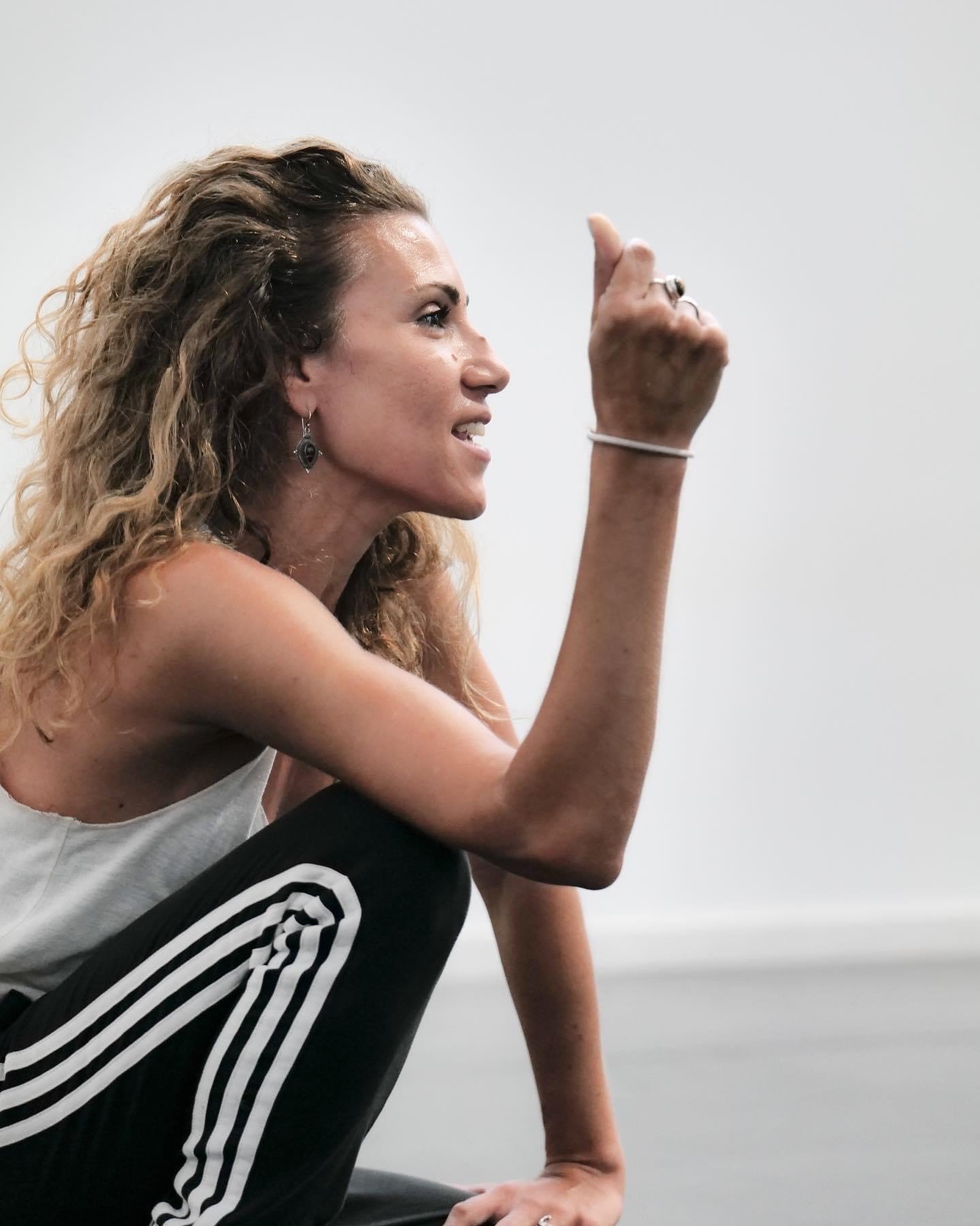 A woman sitting on the floor in a casual outfit, with one hand on the ground and the other hand raised with her middle finger extended, expressing a strong emotion.