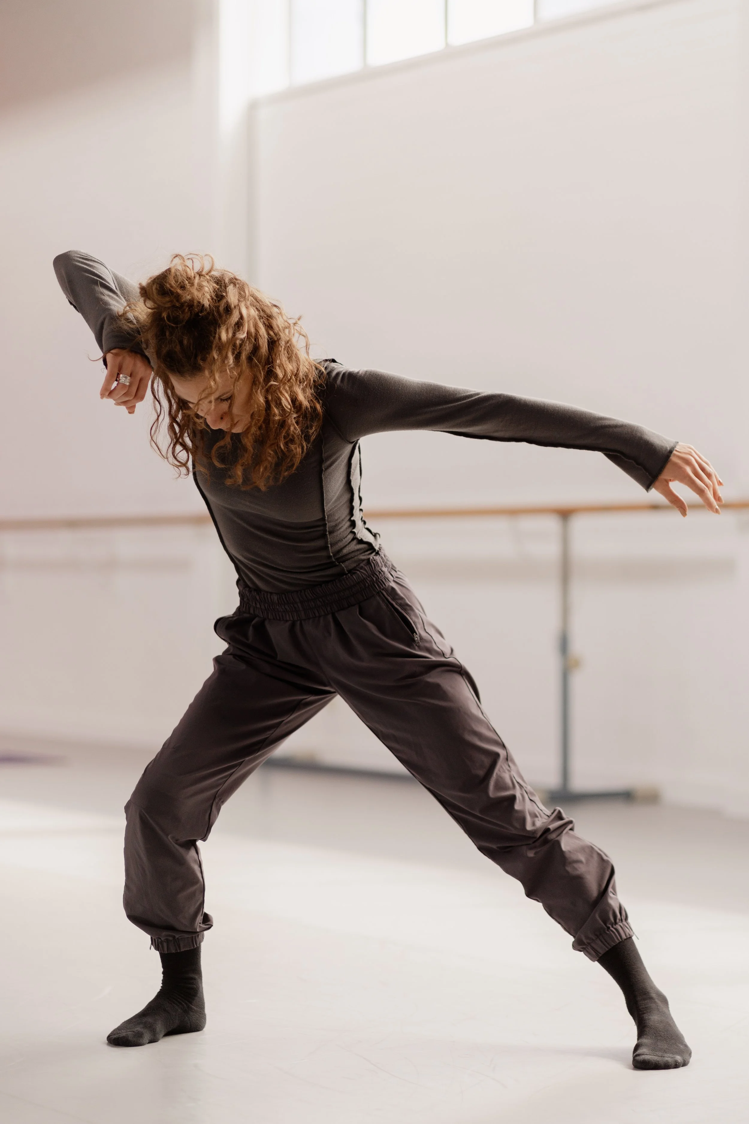 A woman with curly hair practicing dance moves in a dance studio.