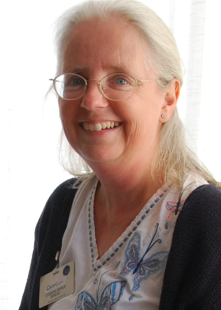Caroline Buxton smiling, who has shoulder length white hair and is wearing glasses, and a black and white top, looking directly at the camera against a white background..