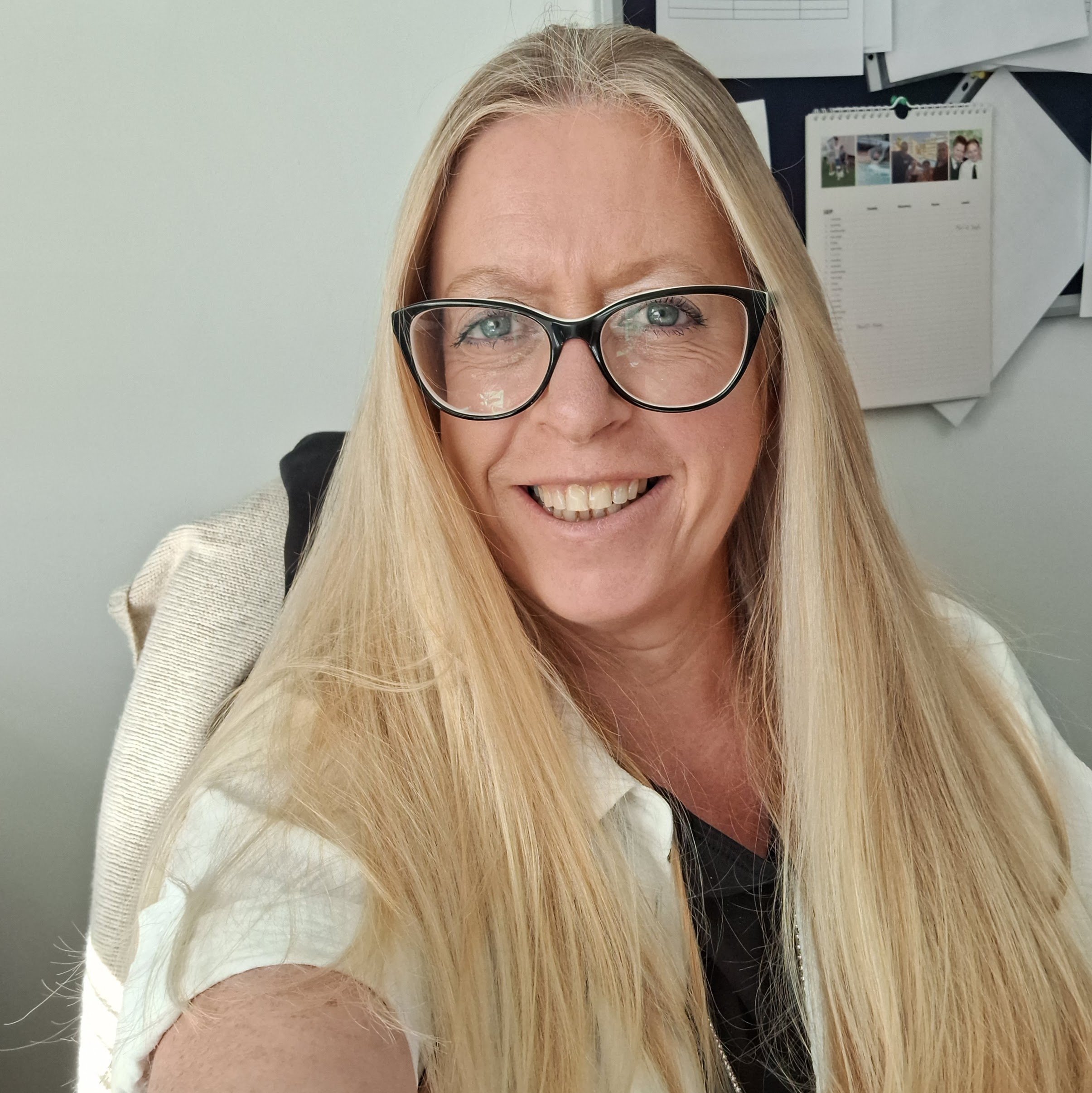 Annie Robson smiling, who has long blonde hair, is wearing glasses, a white top, and is looking directly at the camera against a white background.
