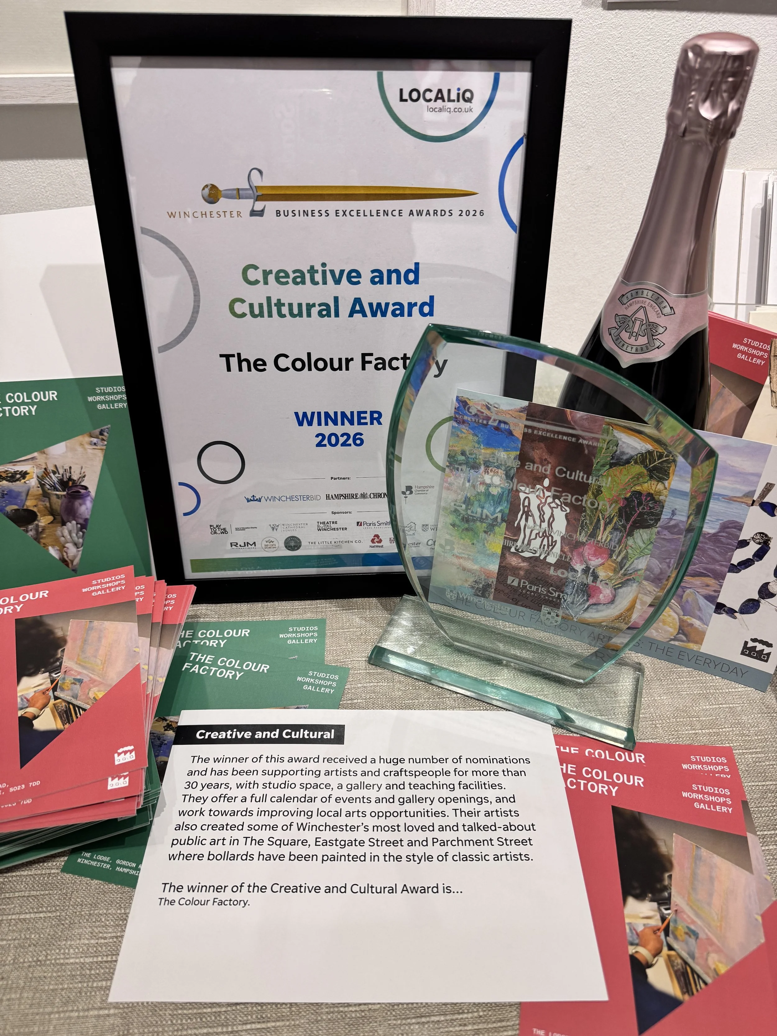 Close-up of The Colour Factory's Winchester Business Excellence Awards 2026 Creative and Cultural Award certificate and glass trophy, with studio postcards and leaflets.