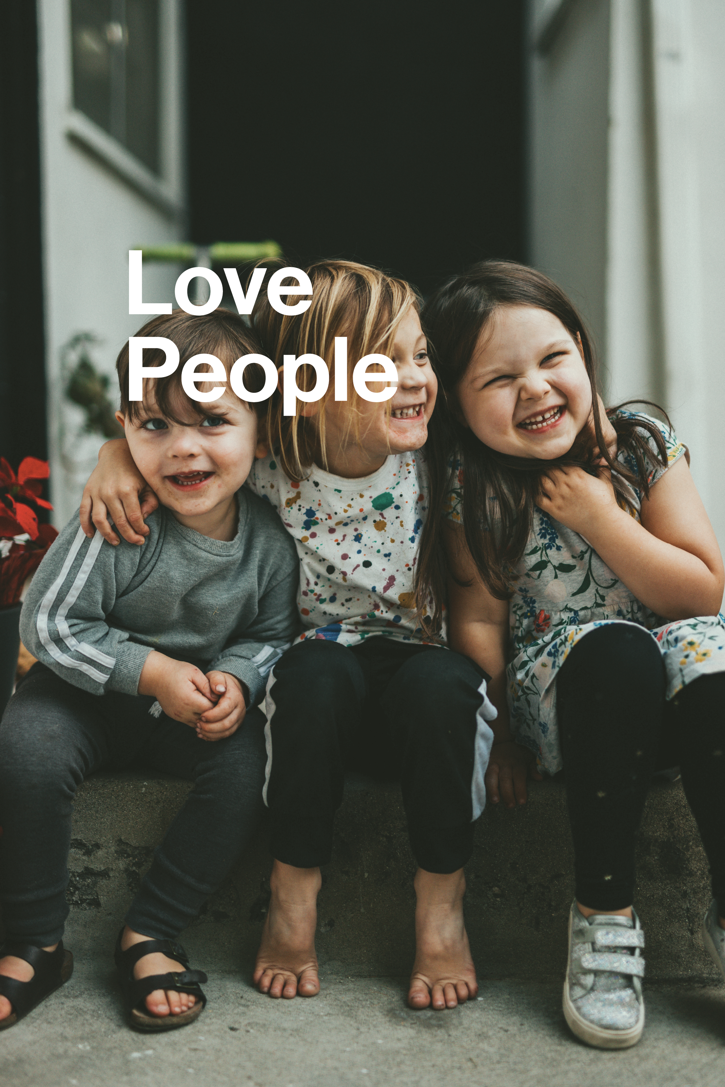 Three young children smiling and hugging each other on a porch, with the text 'Love People' overlaid.