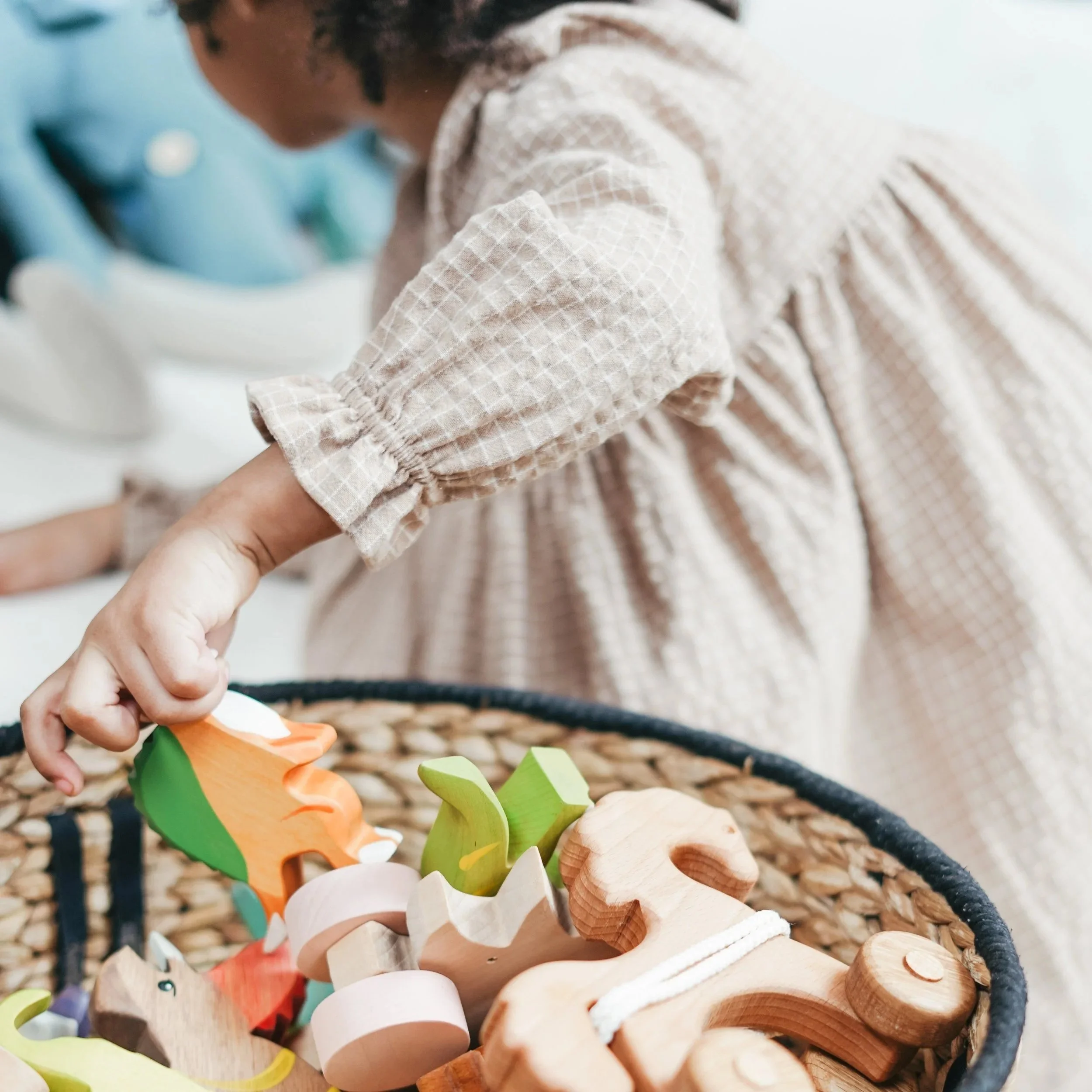Close-up of a child's hand holding a colorful wooden toy, with a background of multicolored wooden toys and a textured surface.
