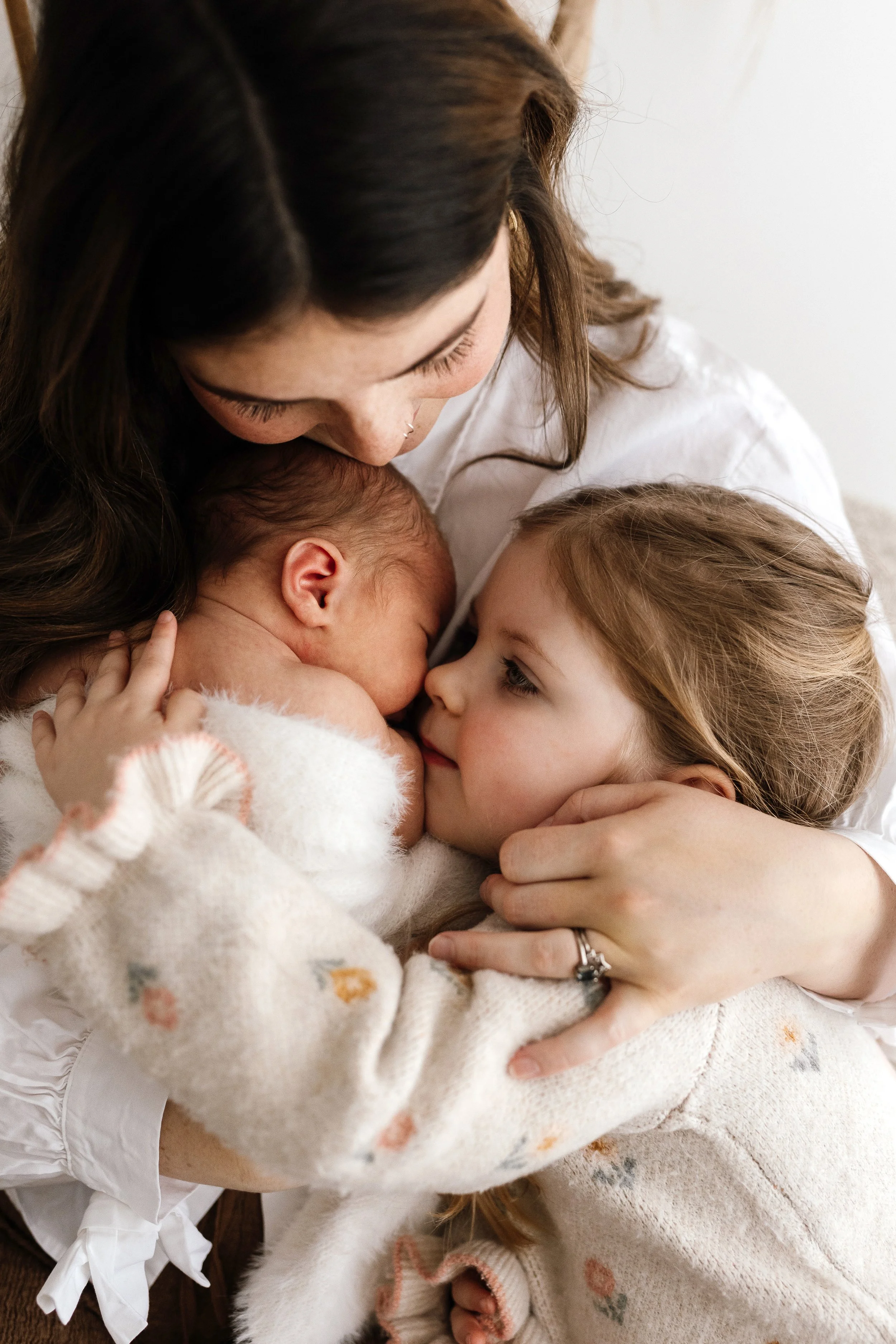 Mother cuddling her newborn baby and young daughter during a relaxed family newborn session