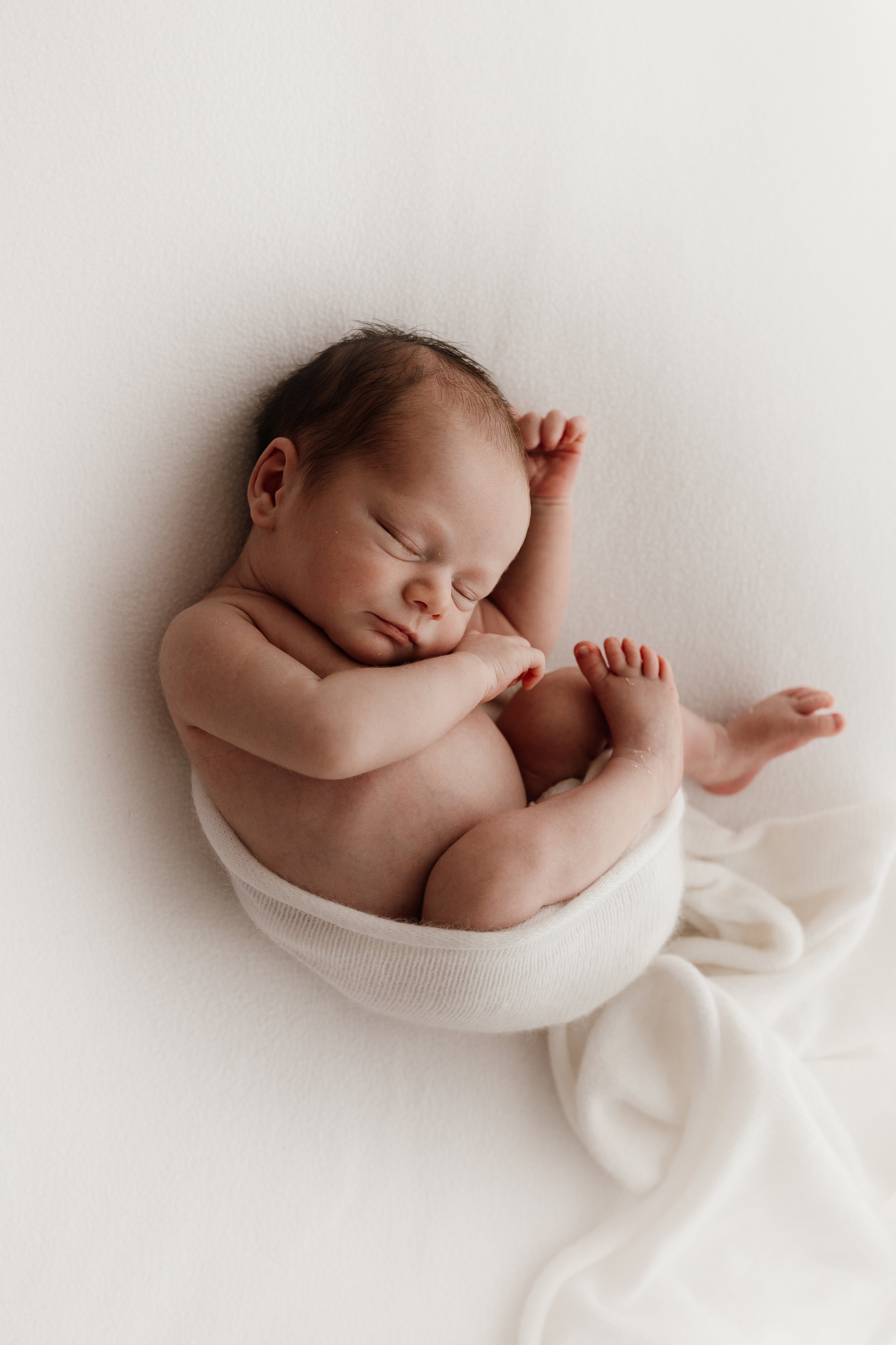 Sleeping newborn wrapped in a soft white blanket on a white background.