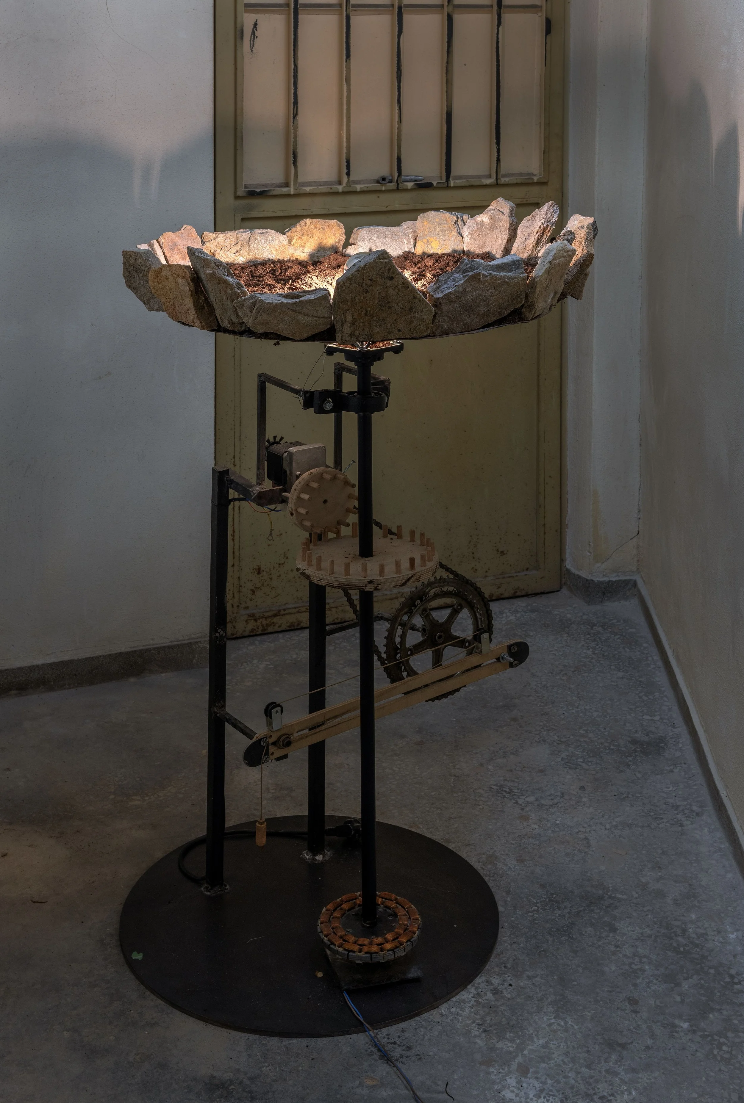 Atzouras (2025)
Spit mechanism, iron, stones,
soil, wood, sheet metal, lamp
110 × 60 × 60 cm
Άτζουρας (2025)
Μηχανισμός σούβλας, σίδερα, πέτρες,
χώμα, ξύλο, λαμαρίνα, λάμπα