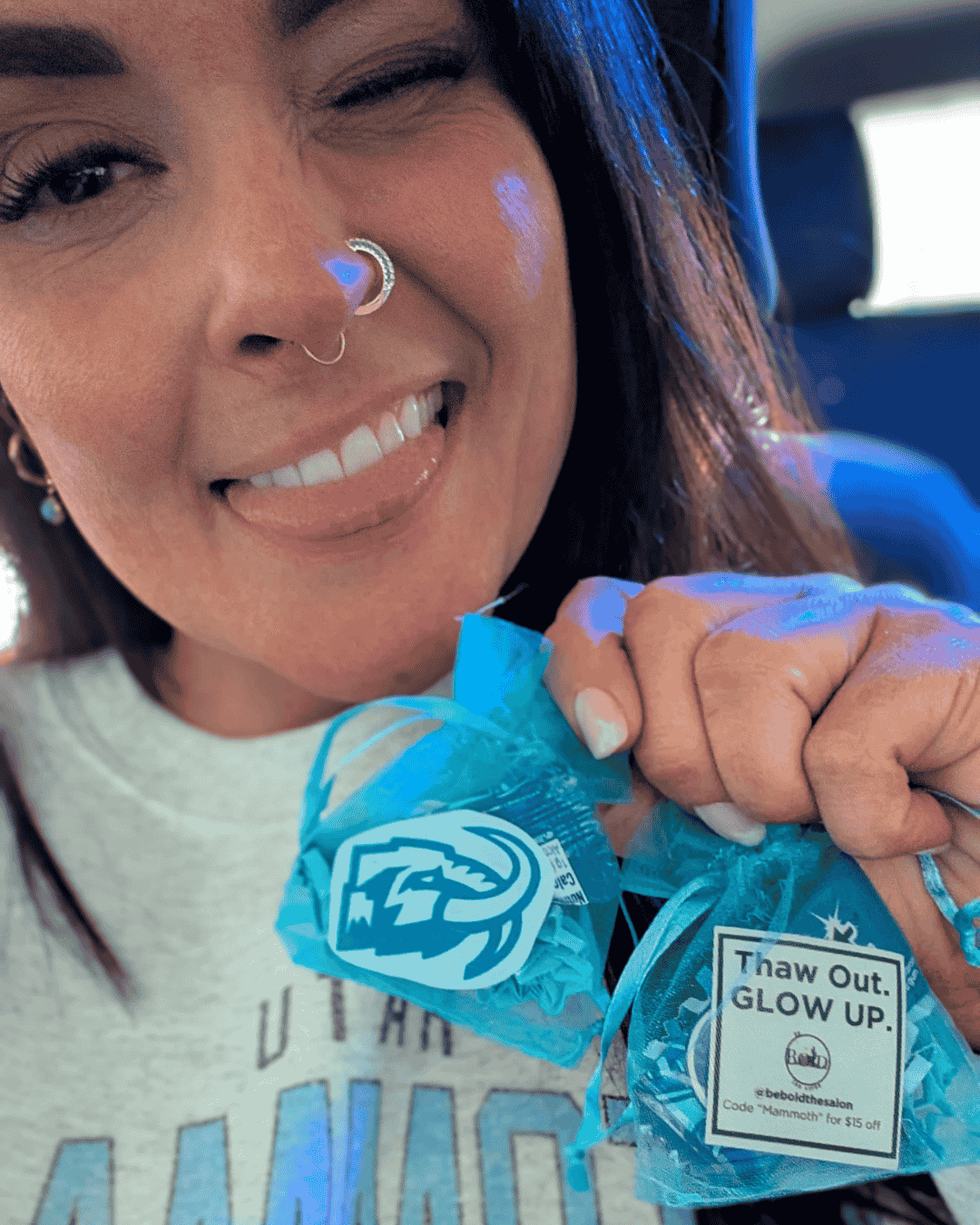 A woman smiling while holding a blue wrapped candy with a logo and a tag that reads 'Thaw Out. GLOW UP.'