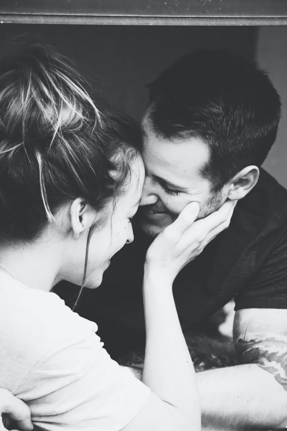 Black and white photo of a couple resting their foreheads together, smiling