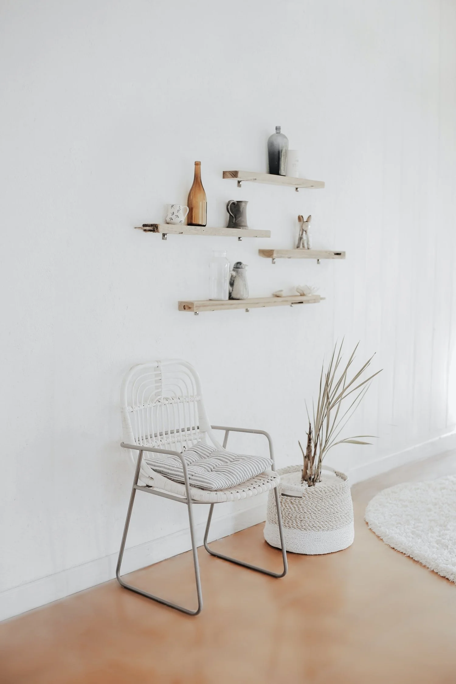 Minimalist living room with wooden shelves, decorative items, a white chair, and a woven basket plant.