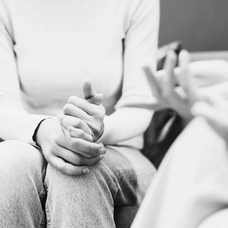 Black and white photo of two people sitting together, one partner's hands clasped around the other's