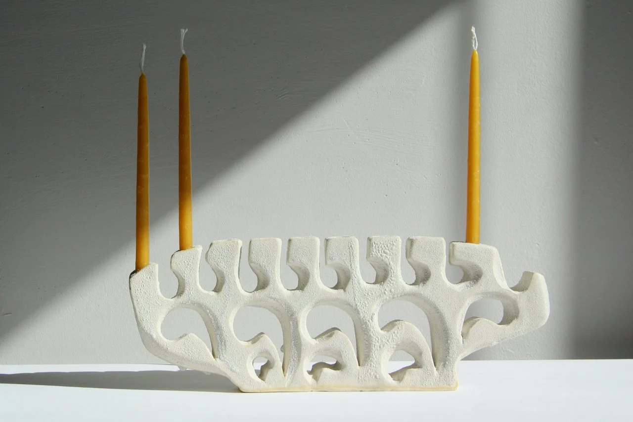 A menorah candle holder with five candles on a white surface, casting a shadow on a plain wall.