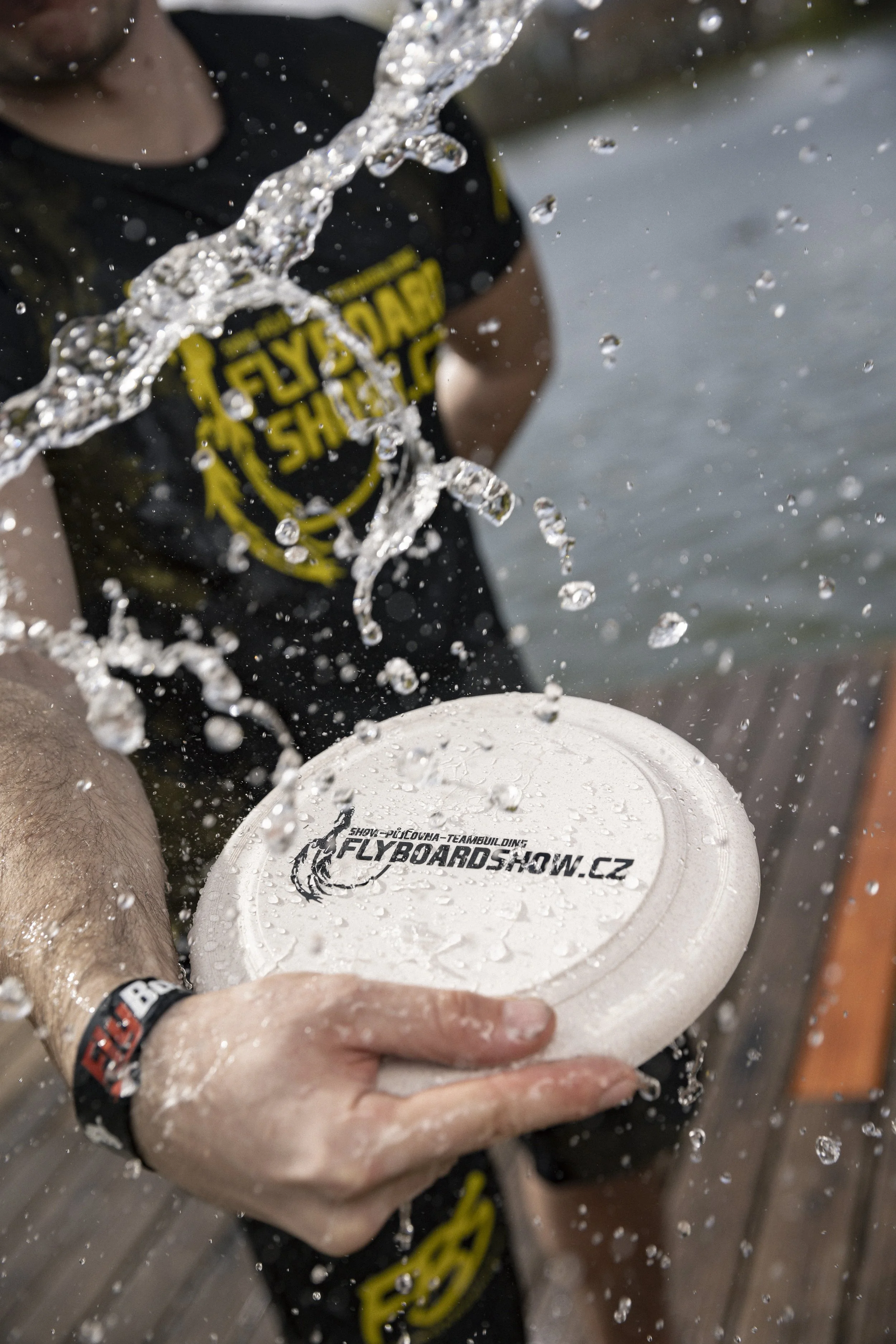 Person holding a white flying disc with a website URL, surrounded by splashing water.