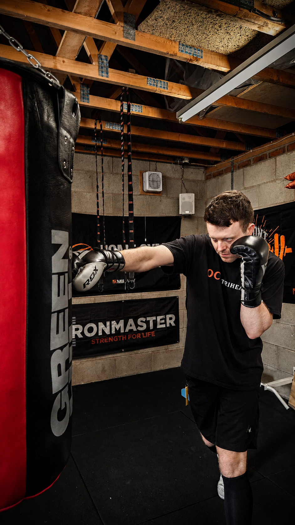 A man practicing boxing in a gym, throwing a punch at a heavy punching bag.