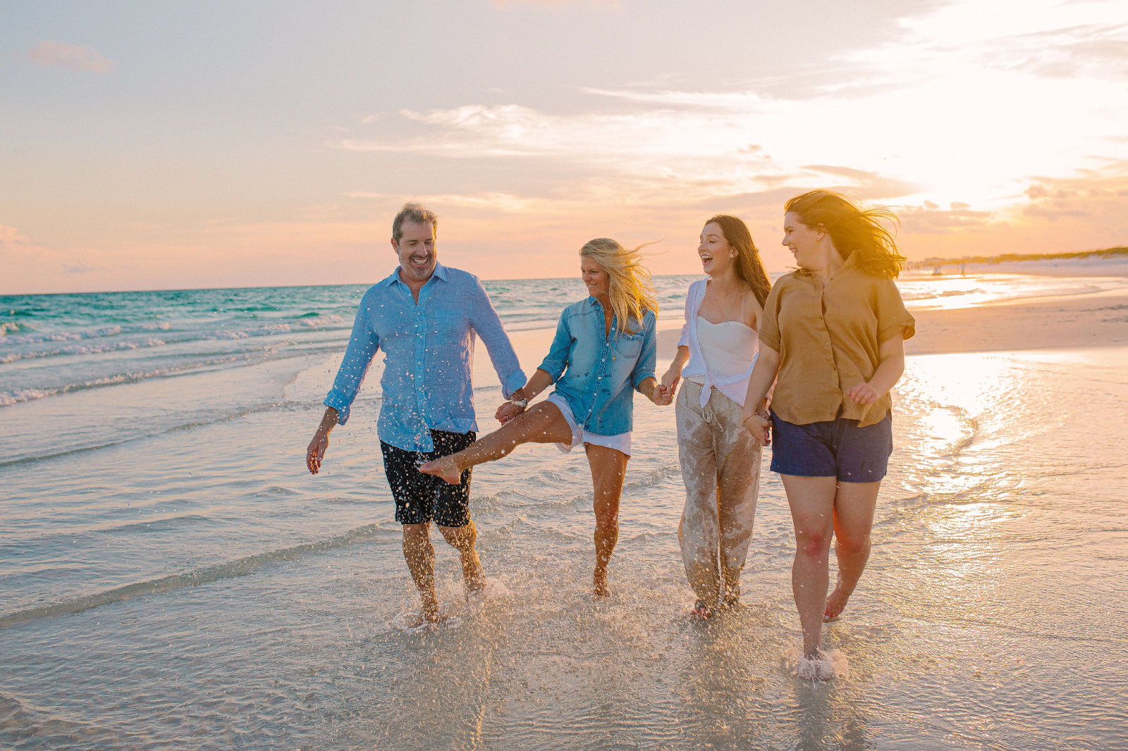 Four people walking in shallow water at sunset.