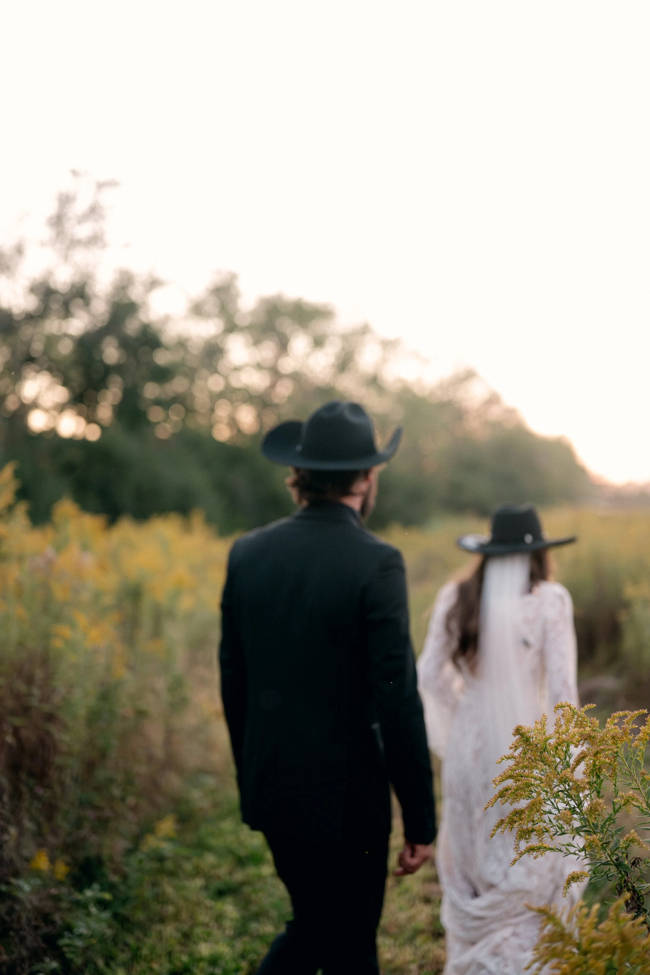 bride and groom walking together through a field of yellow wildflowers at their Honey Farm wedding in Dayton Ohio