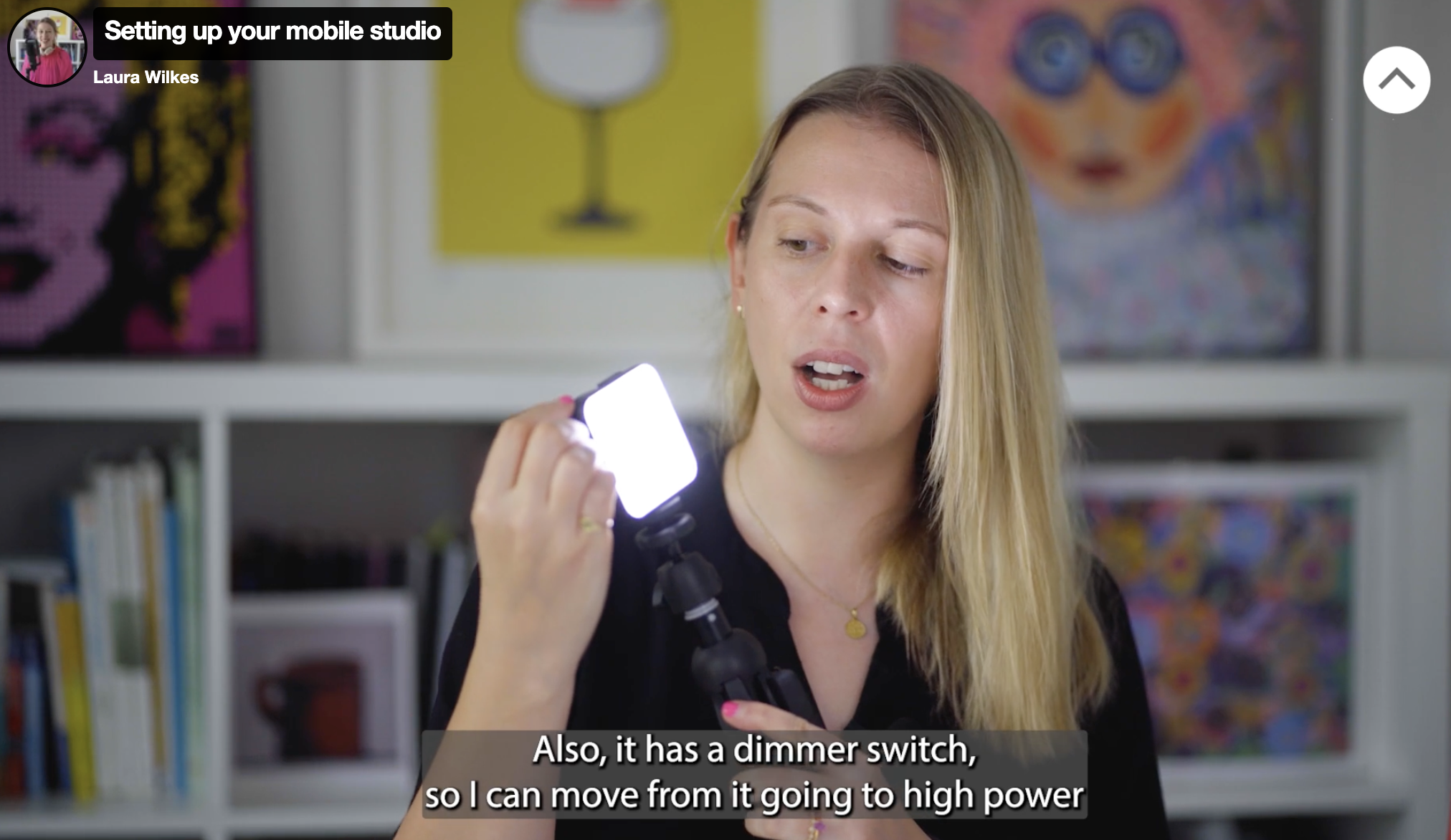 A frame still from one of the many videos on the course. In this frame, Laura is holding up a portable light that you can use in your studio.