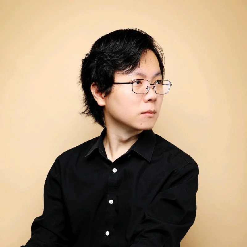 A woman with short black hair, glasses, and a black shirt looking to her right against a beige background.