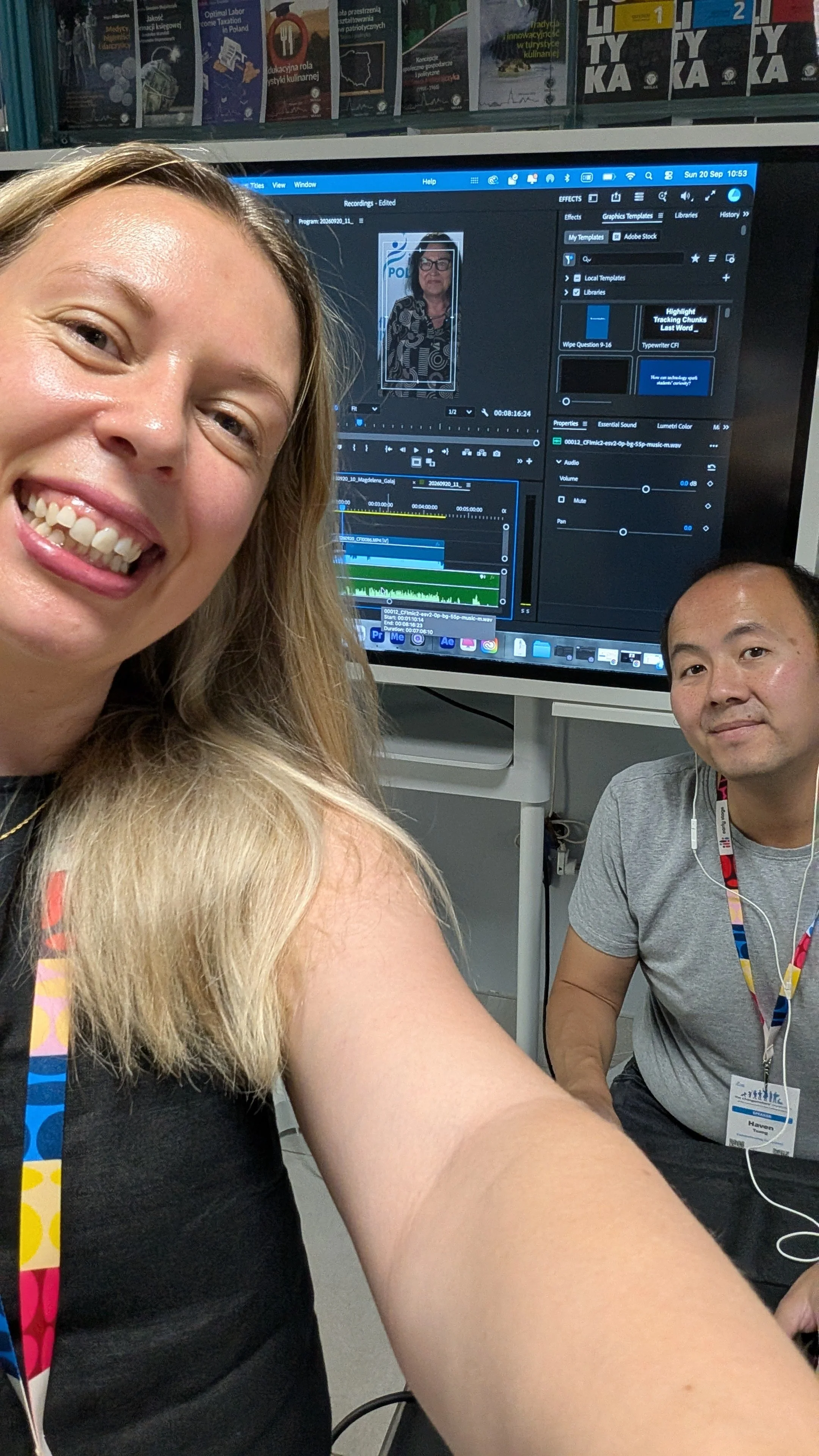 A selfie photo of Laura and Haven editing short vox pop videos they just recorded with attendees at a conference. Laura is holding the camera smiling. Haven is sat behind her at a desk editing with a screen in the background that displays the edit.