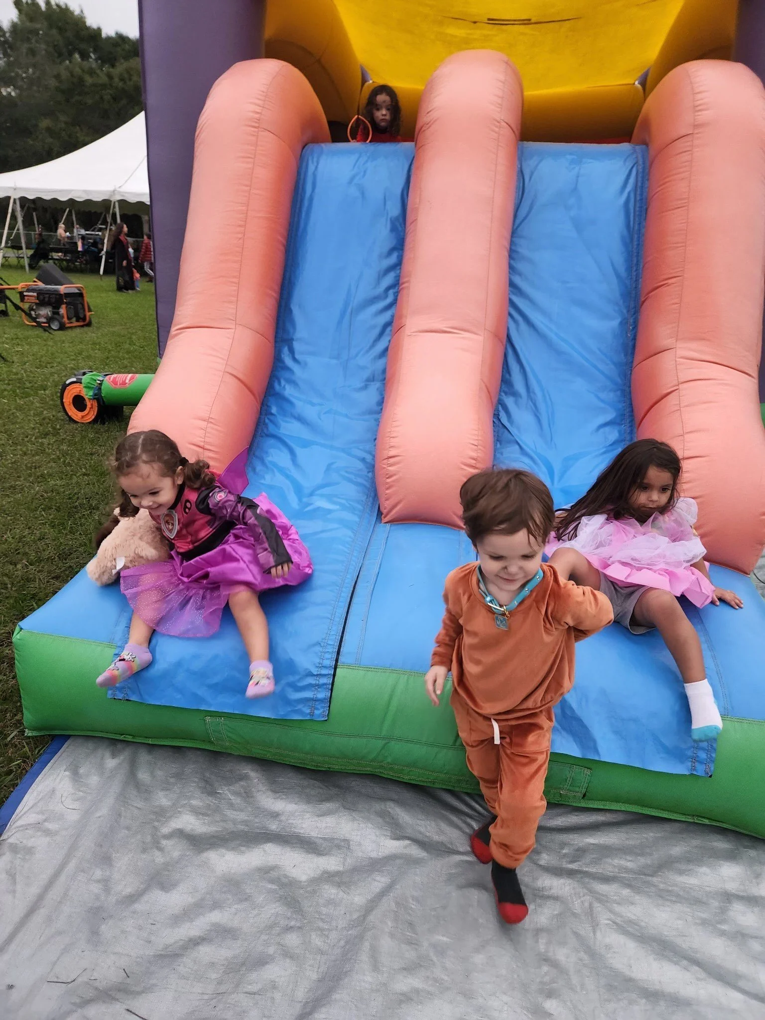 Three children playing on an inflatable slide at an outdoor event.