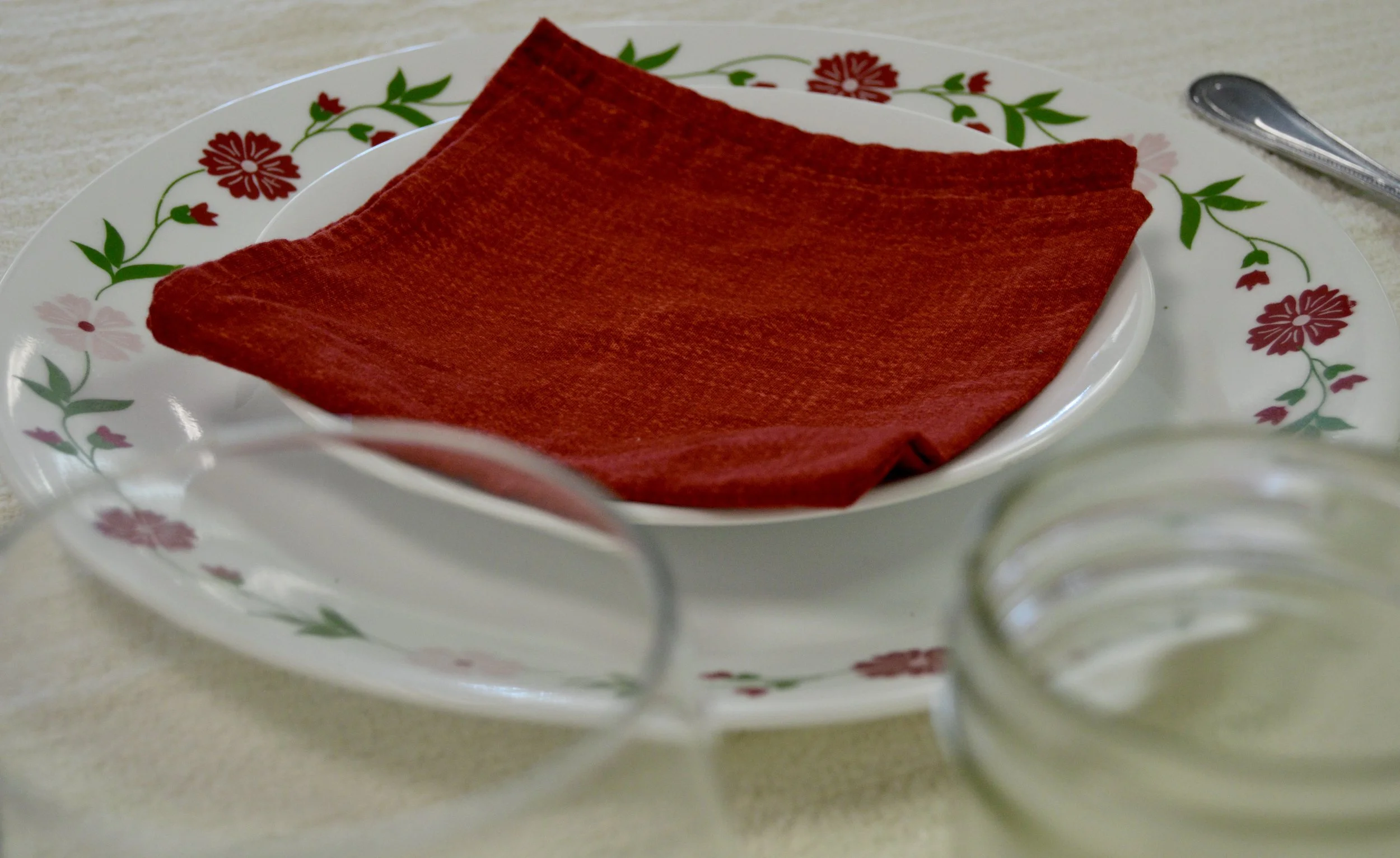 red square napkin set upon dinner setting with red flower design on edge with two glasses in foreground