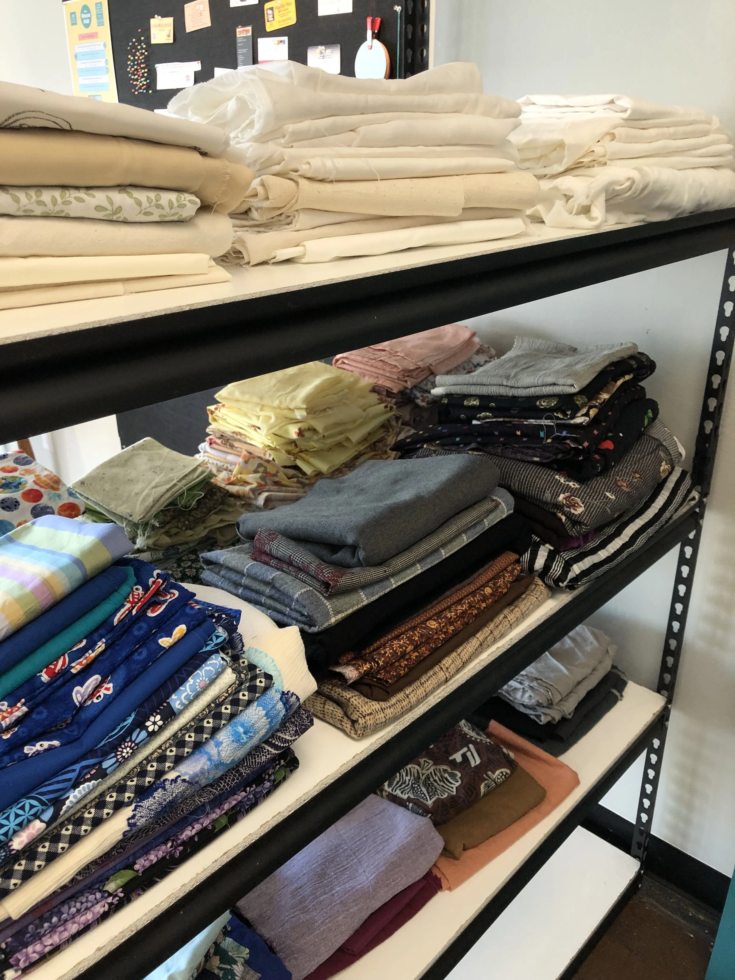Shelving unit with neatly folded fabric and textiles, including sheets, towels, and fabric pieces in various colors and patterns.