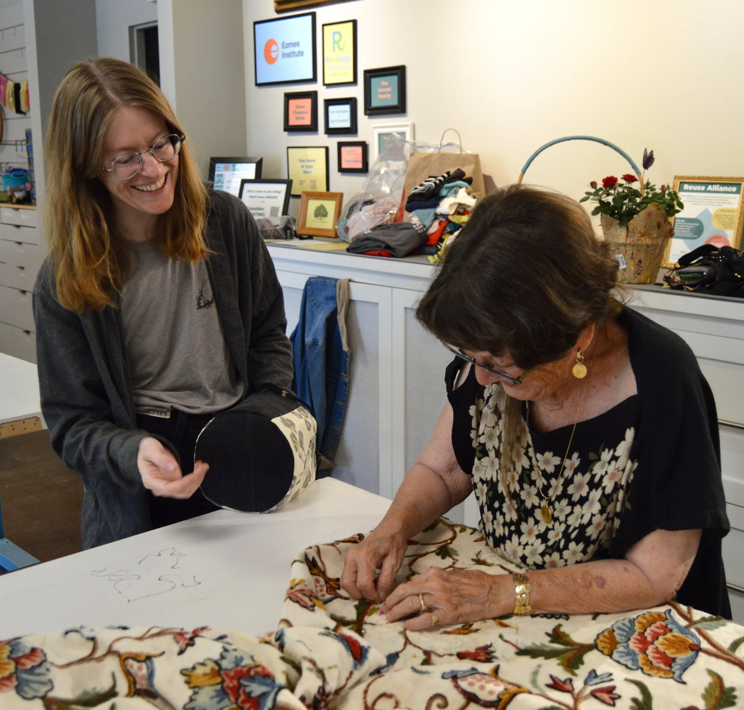 A woman smiling at another woman sewing a large panel of floral fabric