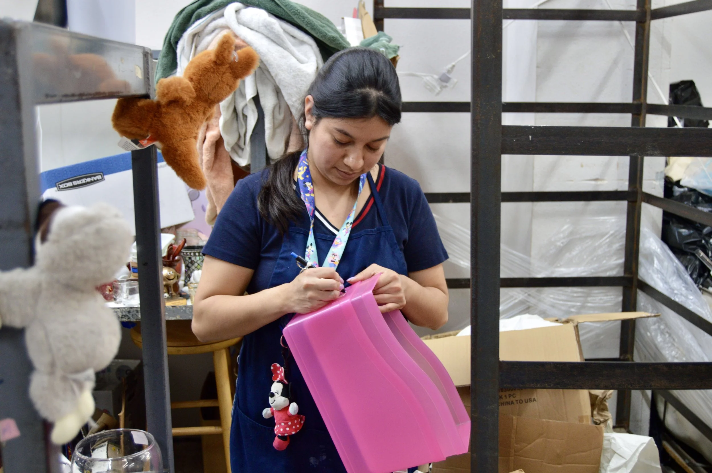 Woman holding bright pink plastic bins writing on its side, bordered by racks.