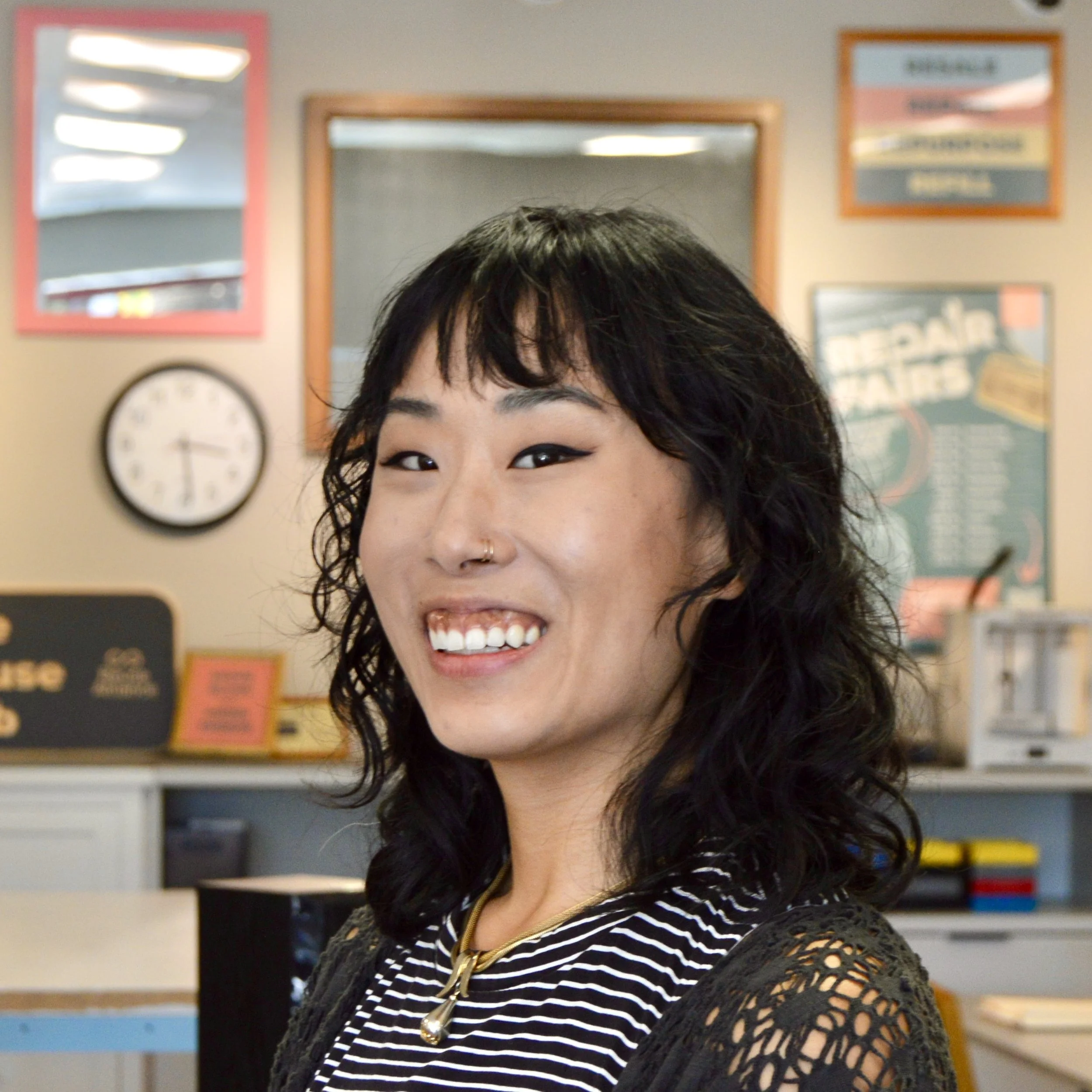 Woman with dark curly hair and bright smile with black and white striped top and colorful framed posters on wall in background