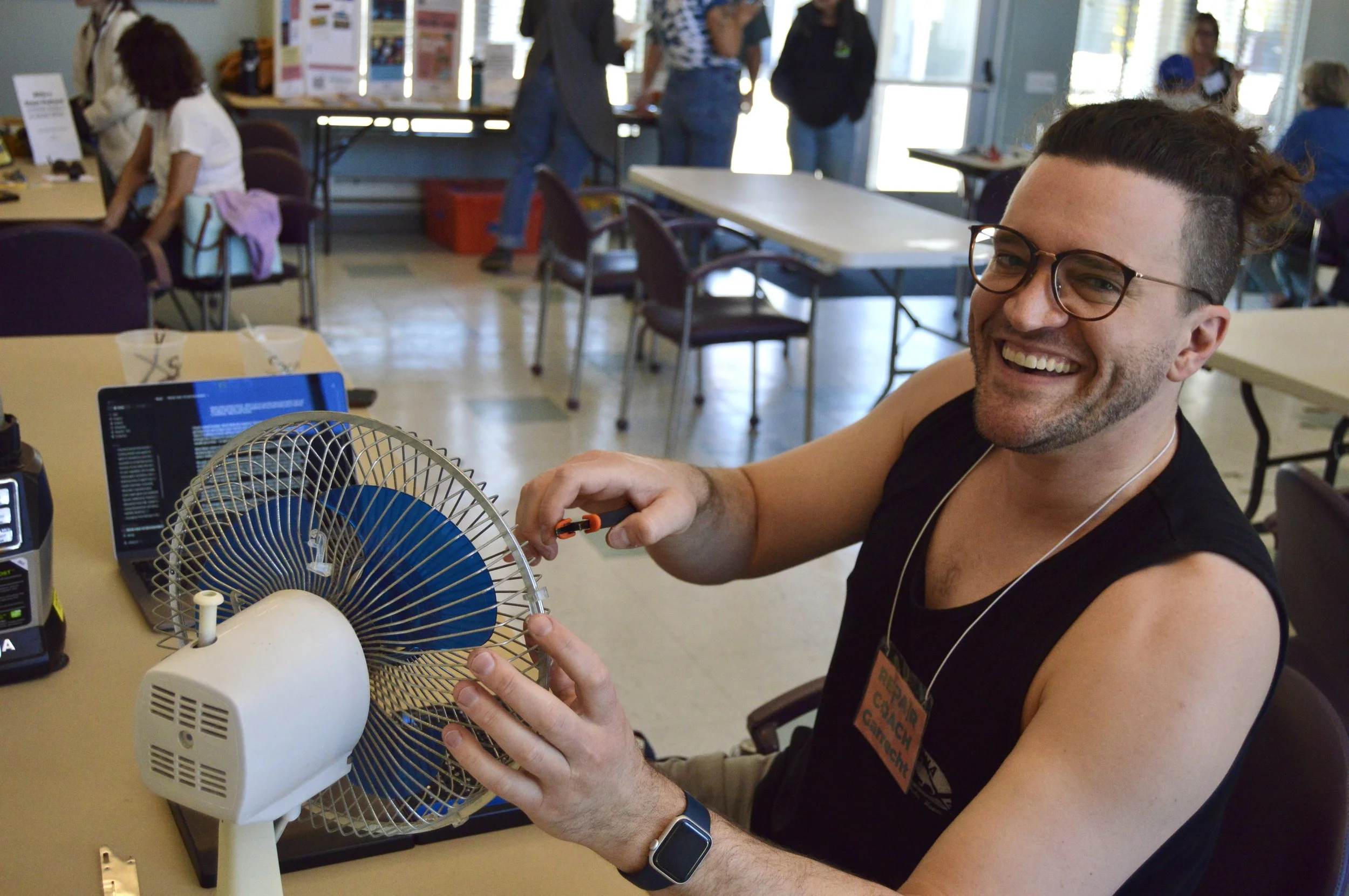 Man looking at camera smiling while repairing a white table fan