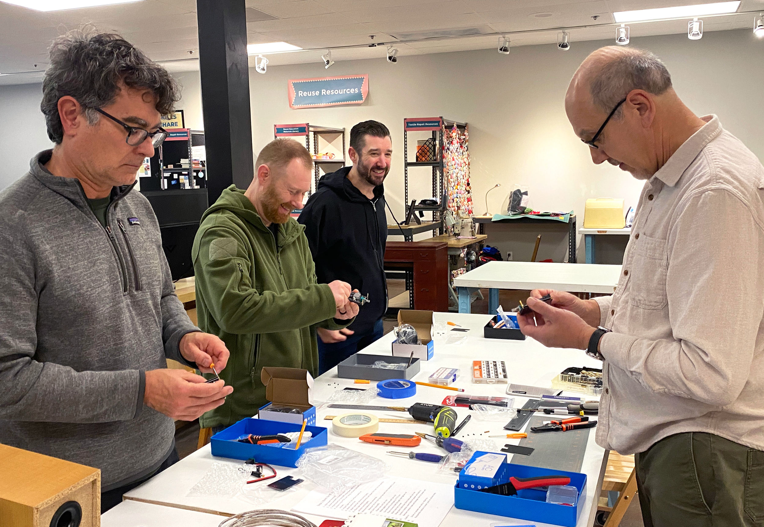 Four men working with their hands in front of a table full of tools