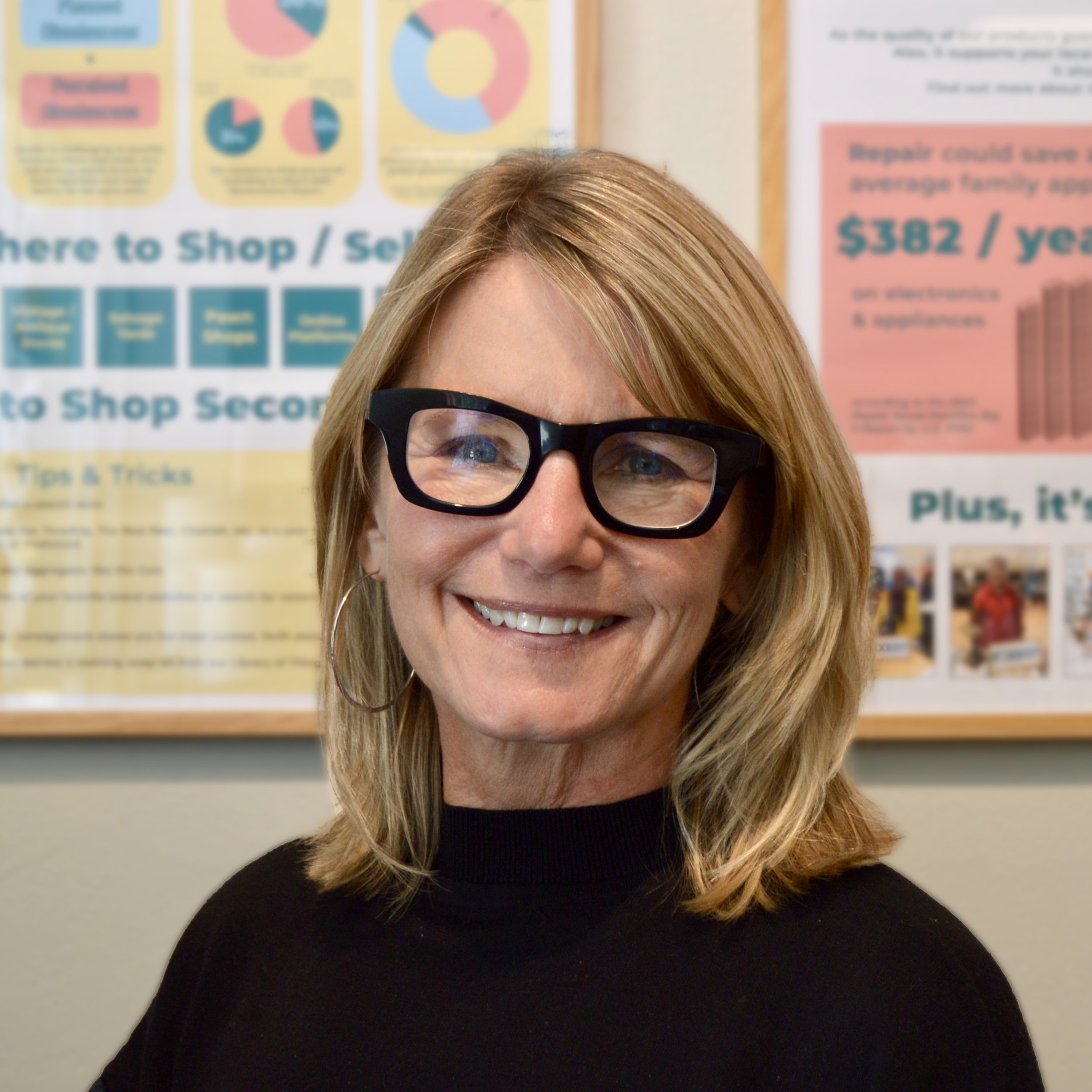 Image of woman with short blonde hair and black turtle neck sweater with black glasses in front of posters