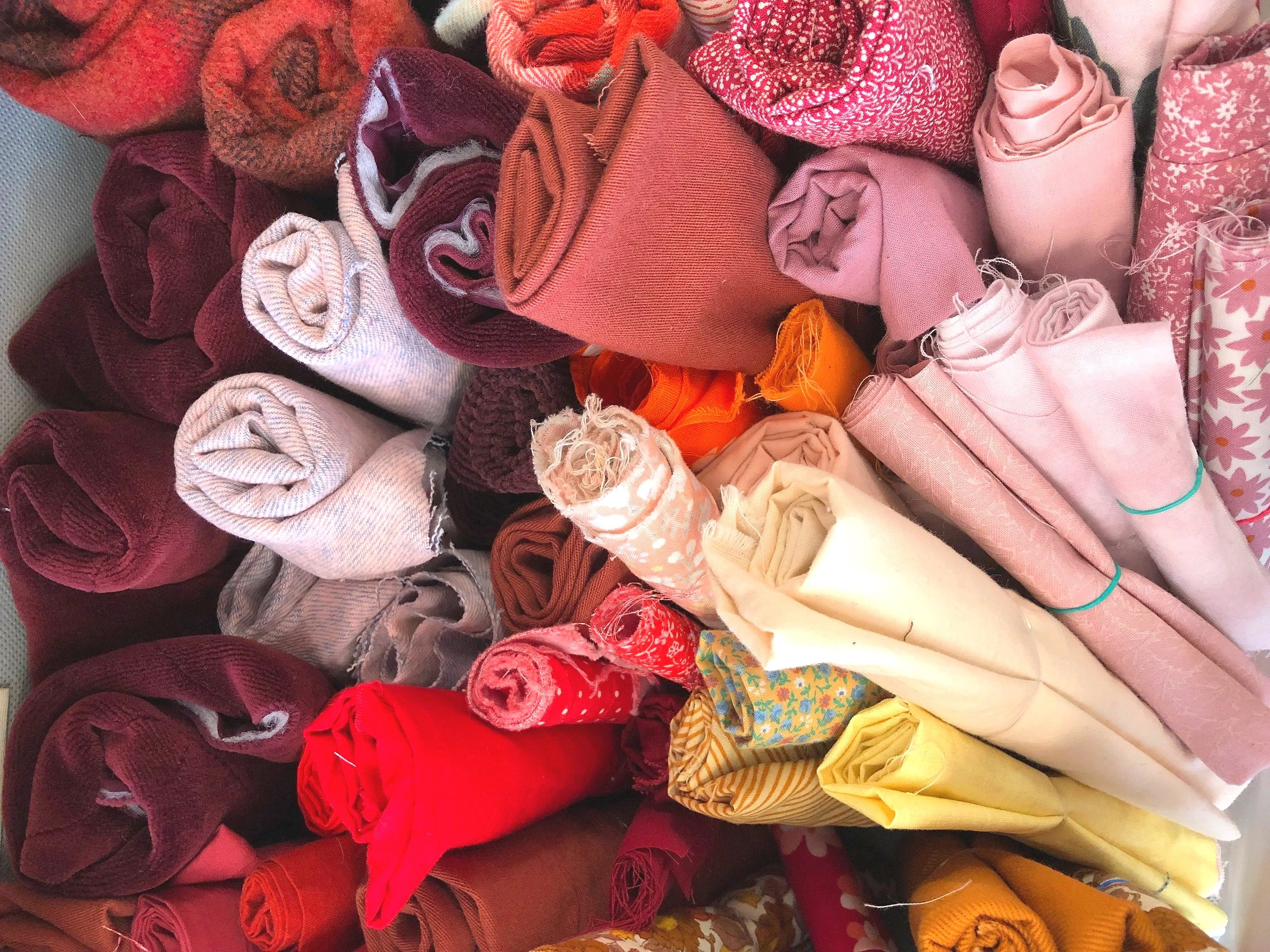 A collection of rolled-up fabrics in various colors including red, pink, orange, purple, yellow, and patterned textiles.