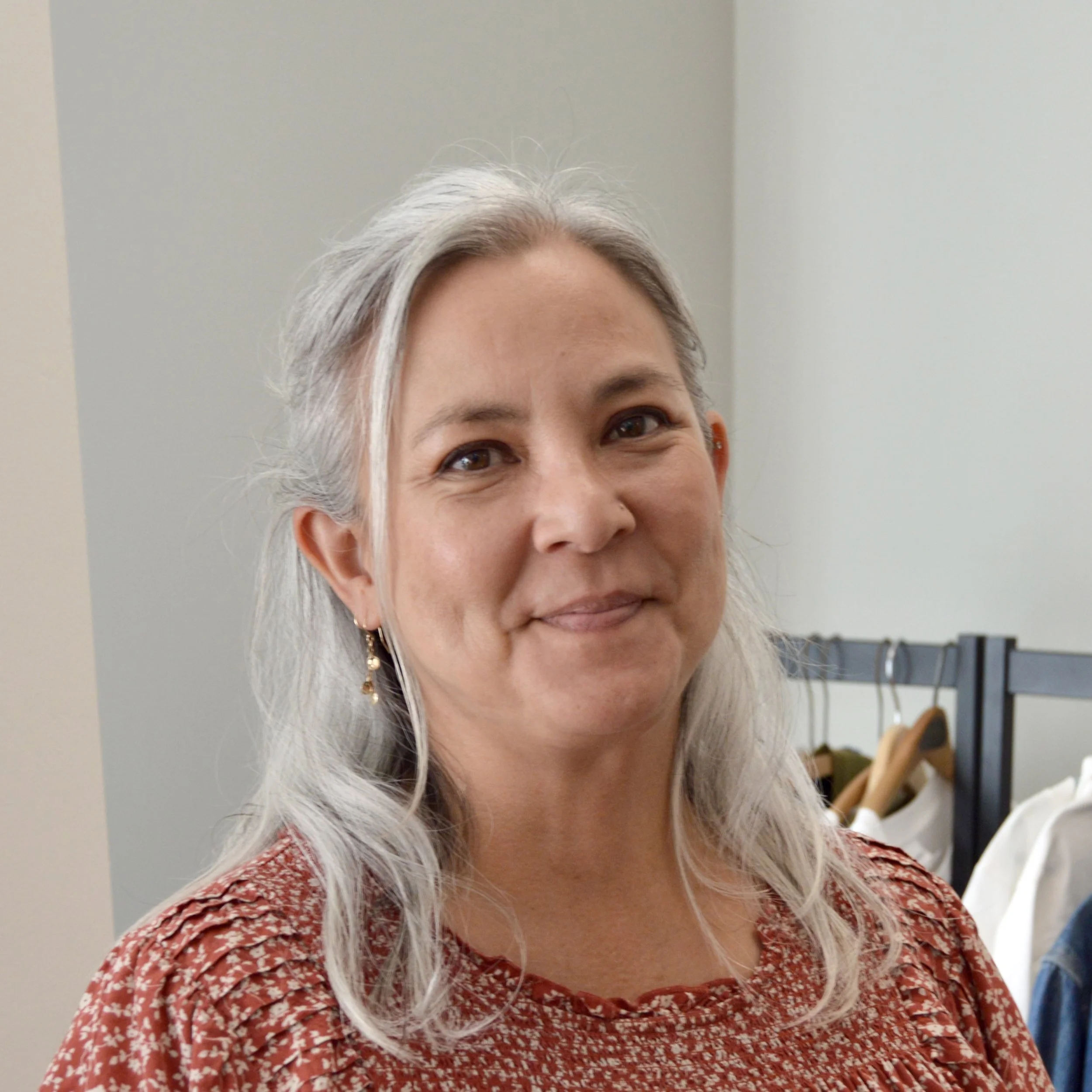 Women with closed mouth smile wearing red top with white flowers with grey walled background