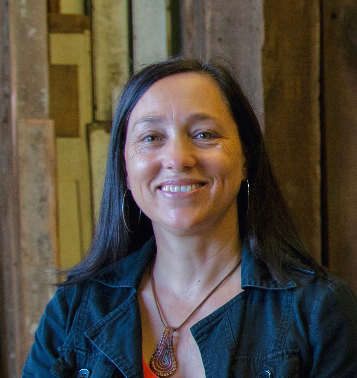 A woman with dark long hair with bright smile in front of wooden panel background