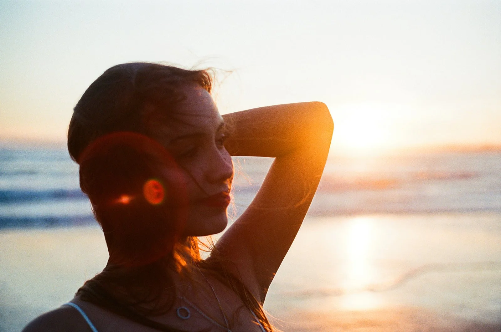 Woman with closed eyes at the beach during sunset, her hand resting behind her head.