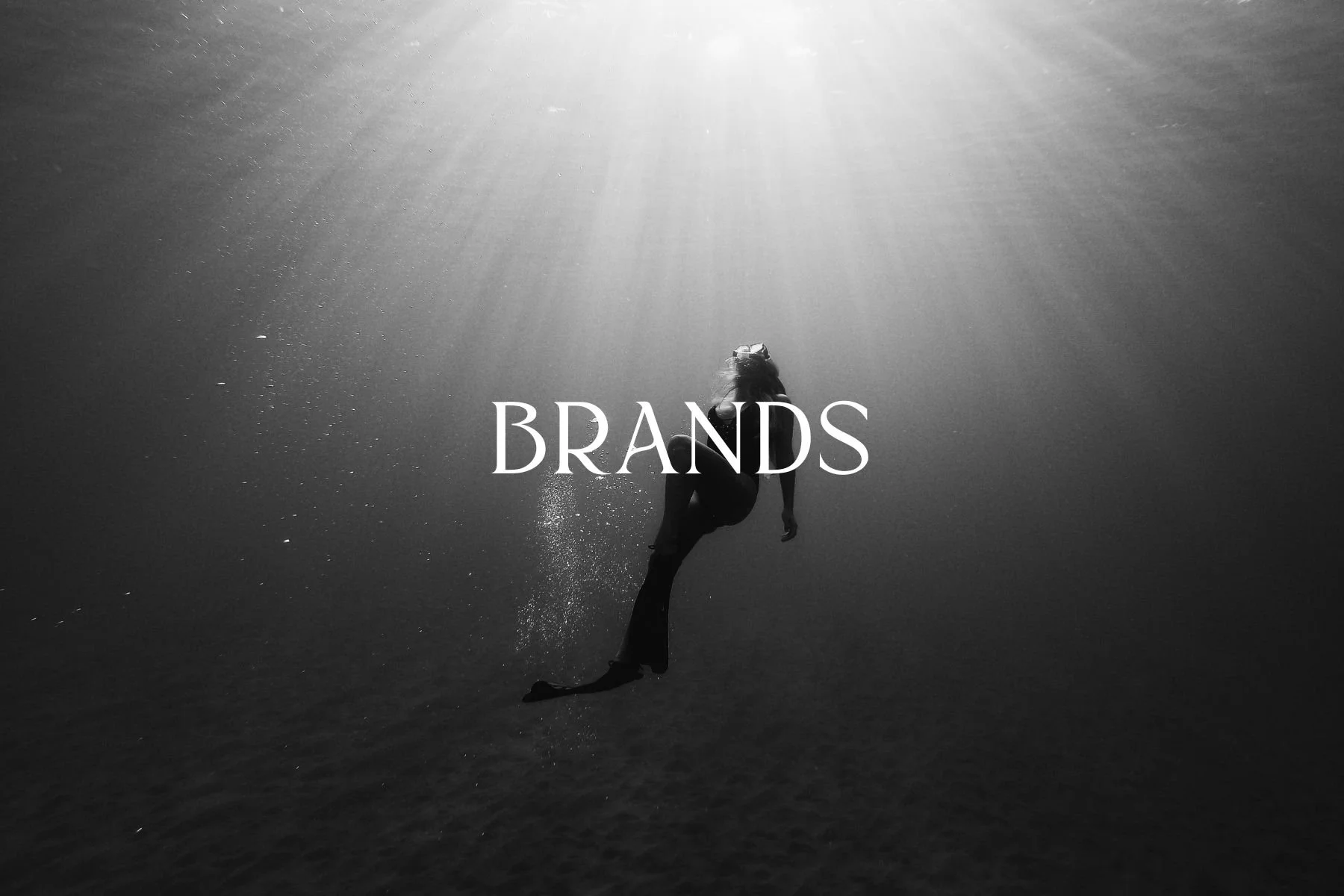An underwater scene in black and white showing a person swimming towards the surface, with sunlight streaming down and the word 'BRANDS' overlaid in the center.