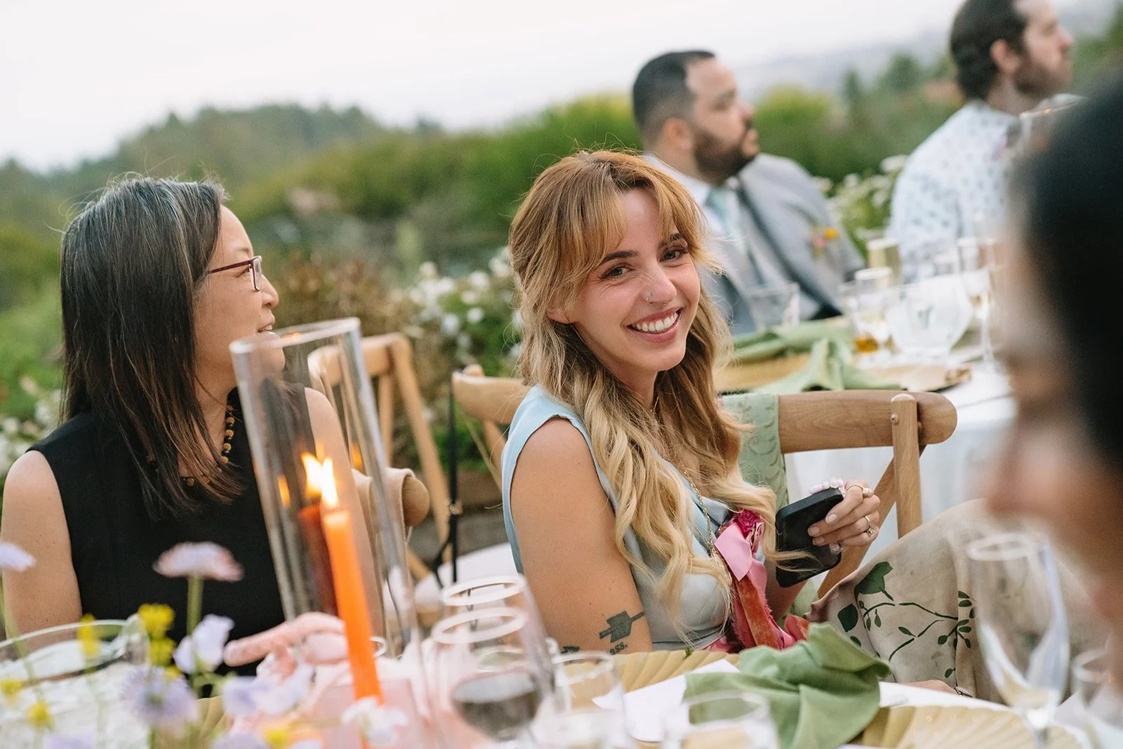 People sitting at a table outdoors during a celebration, smiling and enjoying the event.