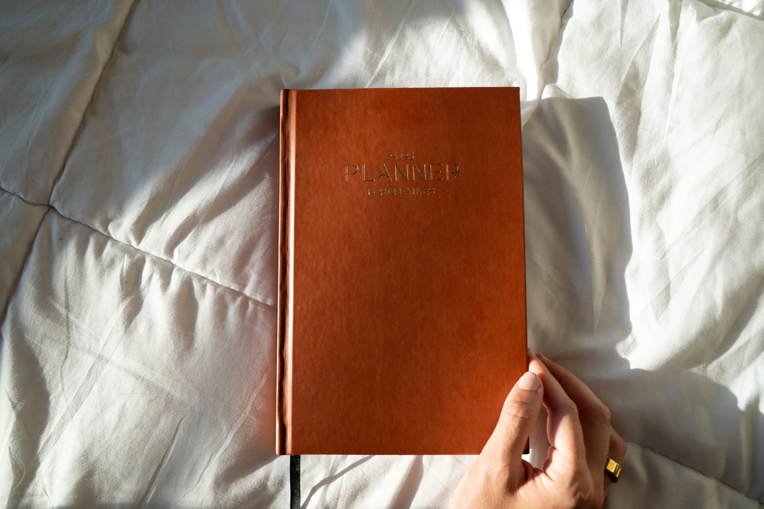 A hand holding a 2023 planner with a brown cover on a white textured fabric surface.