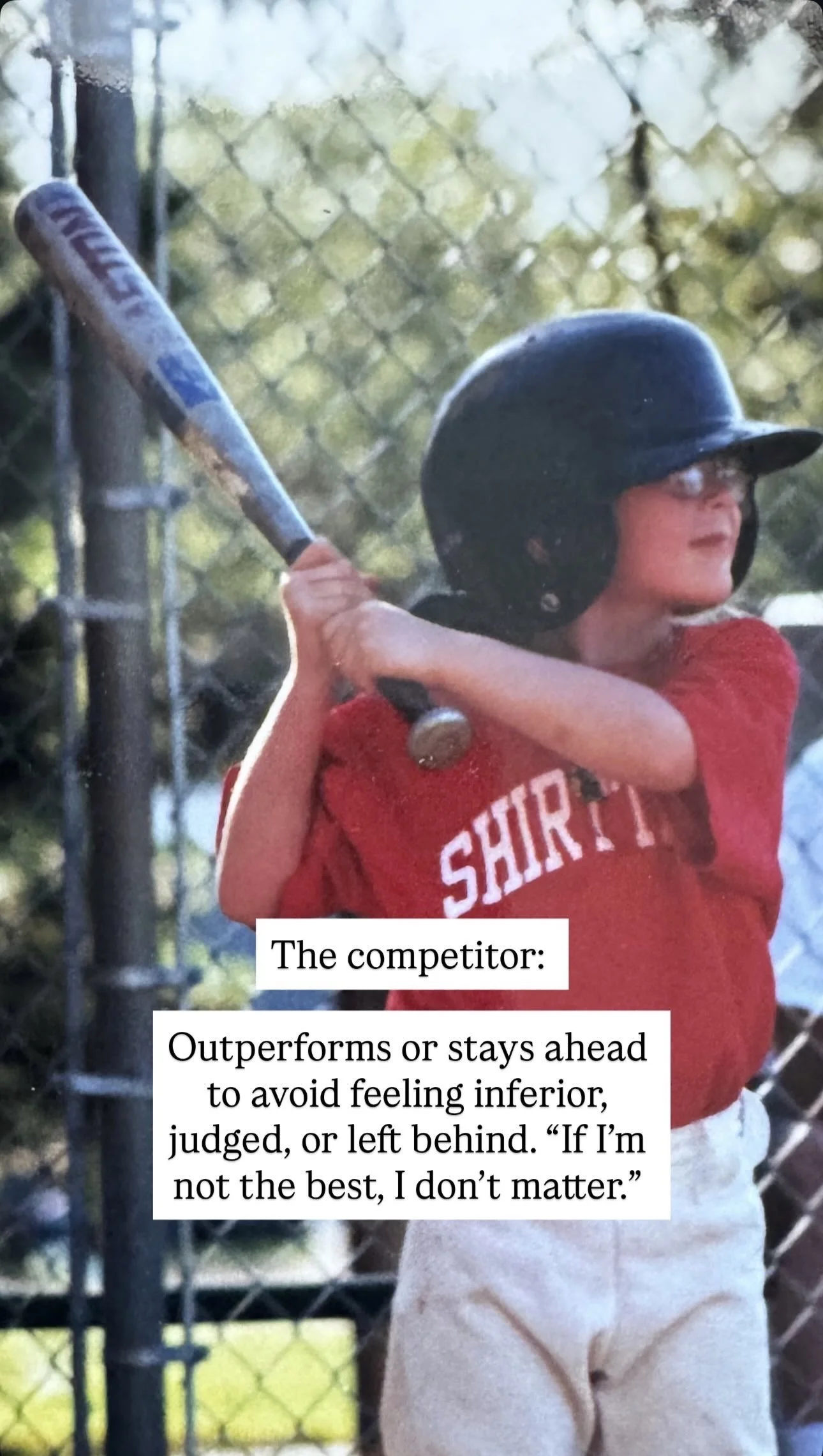 A young boy wearing a red shirt with 'SHIRT' written on it, a black baseball helmet, and white pants, holding a baseball bat prepared to swing during a game at a baseball field with a chain-link fence in the background.