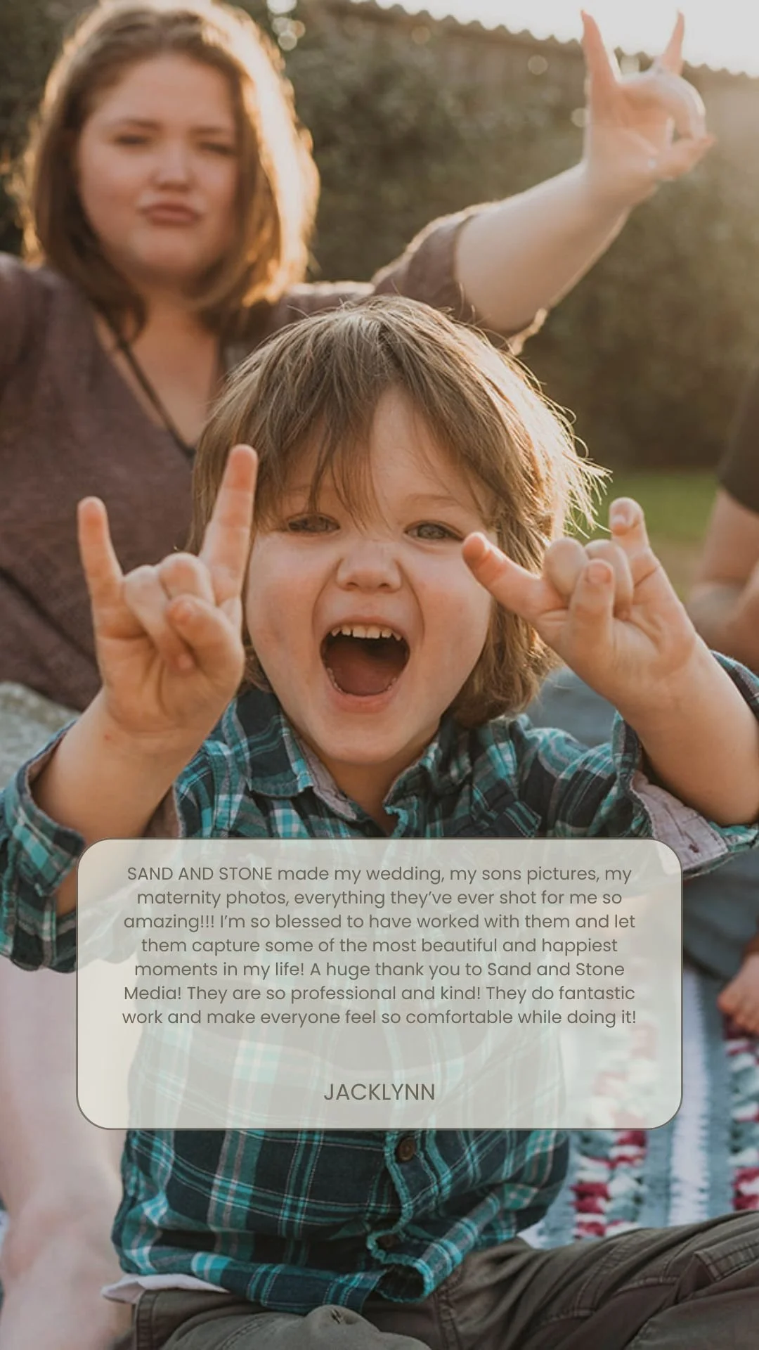 A young boy with brown hair, wearing a checkered shirt, making rock on hand gestures with his mouth open in excitement. Behind him, an adult woman with shoulder-length hair makes a similar hand gesture, blurred in the background, during sunset outdoors.