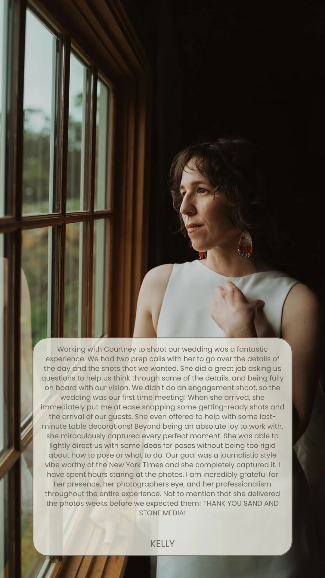 A woman with short dark hair and earrings, standing by a window, gazing outside.