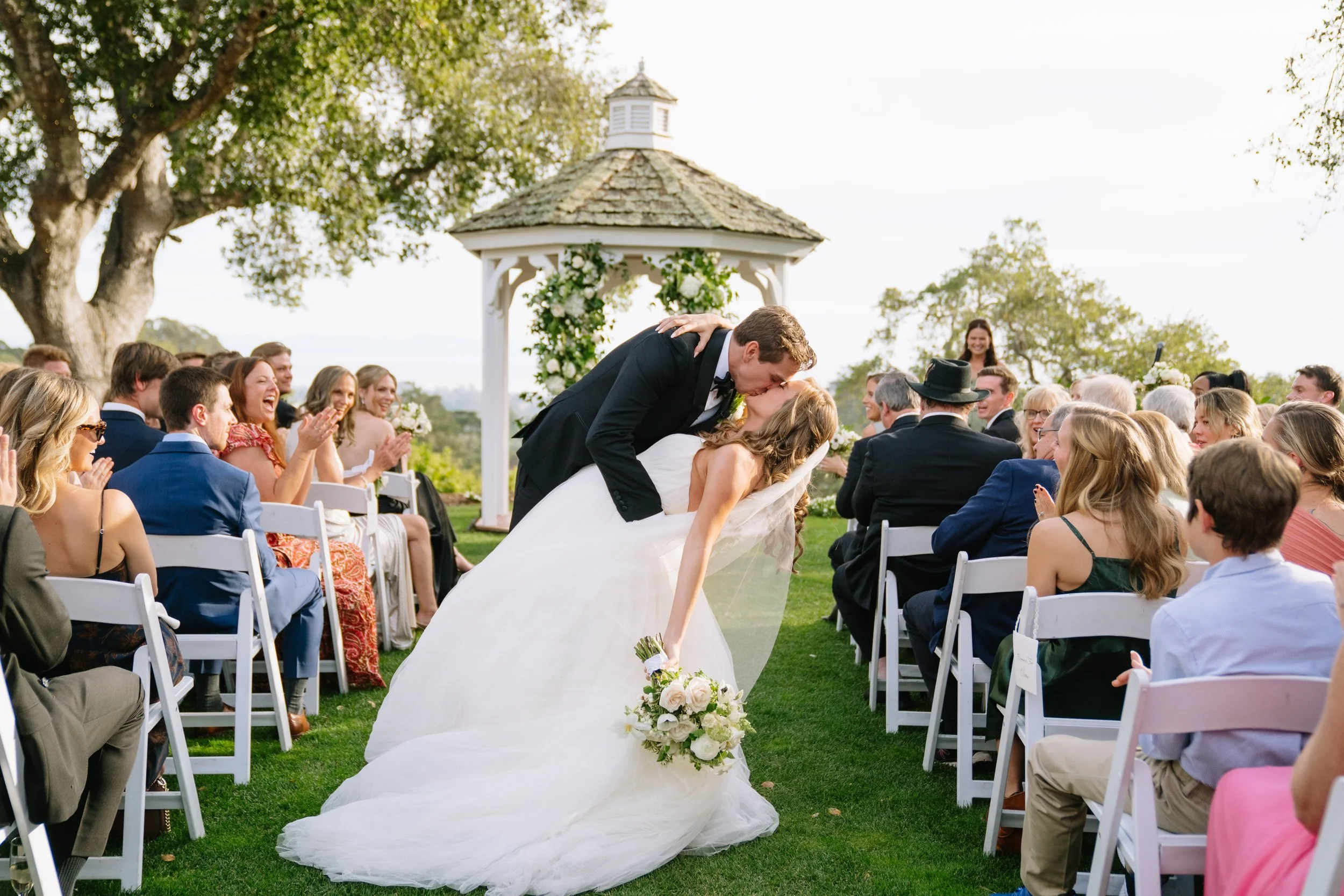 Bride and groom kissing at their outdoor wedding ceremony surrounded by guests