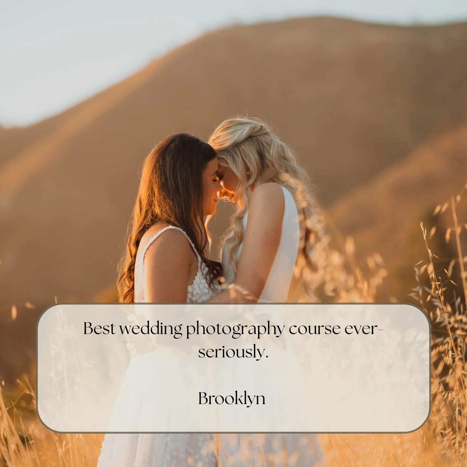 Two women, dressed in wedding attire, touching foreheads in a field at sunset with mountains in the background.
