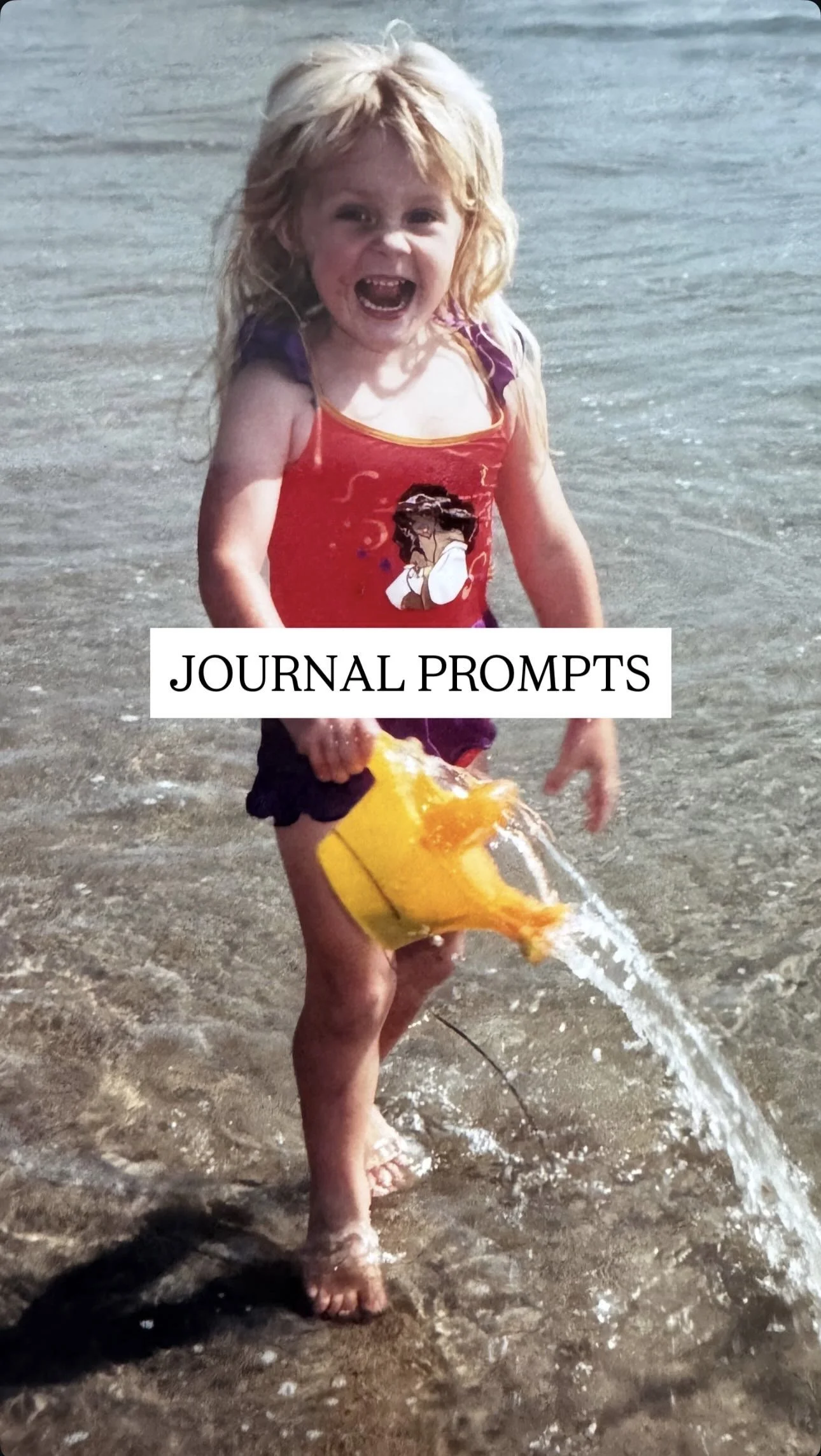 A young girl with blonde hair, wearing a red and purple swimsuit, is playing at the beach with a yellow toy bucket, pouring water.