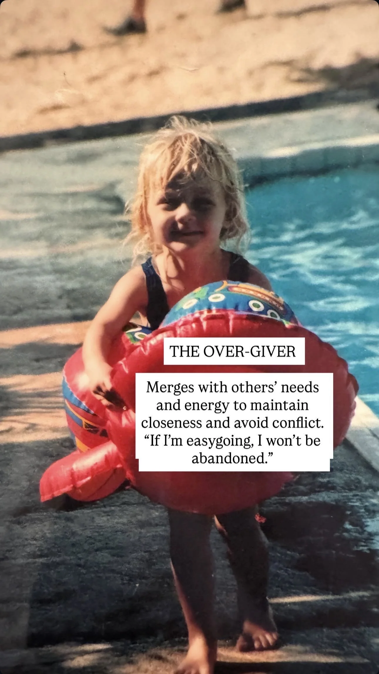 A young girl with blonde, wet hair in a swimming pool, holding onto a colorful inflatable ring, with a sandy edge and water ripples in the background.