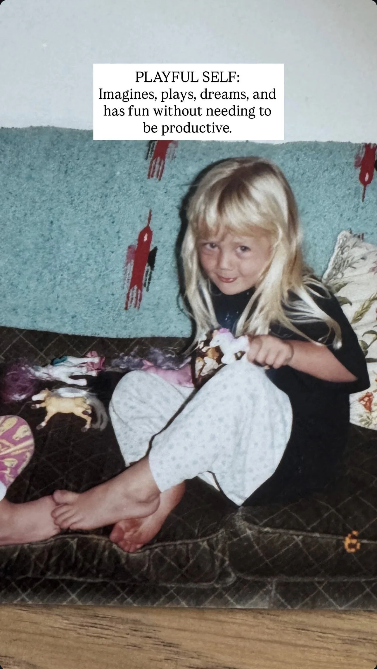 A young girl sitting on a couch, smiling, holding a small unicorn toy, with a blue and brown couch, and a pillow behind her.