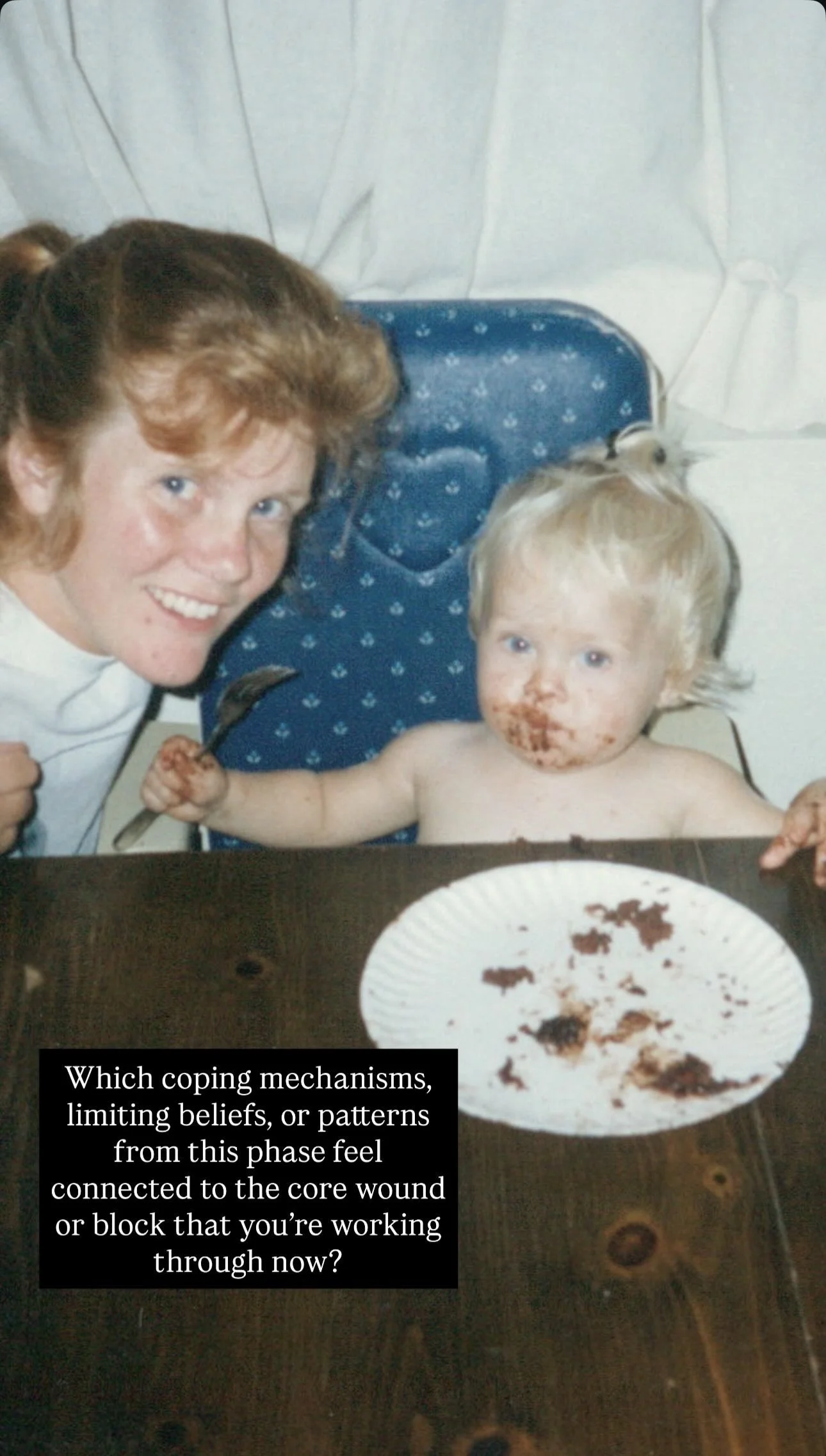 A woman with red hair leaning over a wooden table, smiling at a young child with blonde hair sitting in a high chair. The child has a messy face with chocolate and is holding a fork. A paper plate with leftover chocolate is on the table, and there is