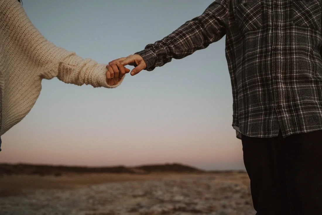 Close-up of two people holding hands outdoors during sunset.