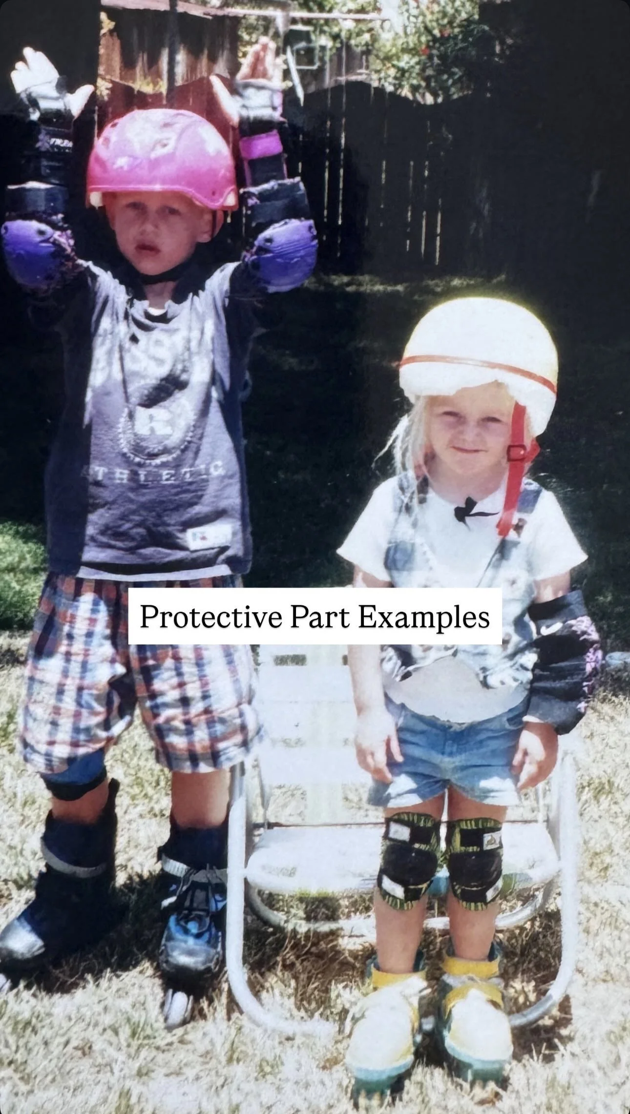 Two children wearing protective helmets and knee pads, standing outdoors on a chair, with a wooden fence and trees in the background.