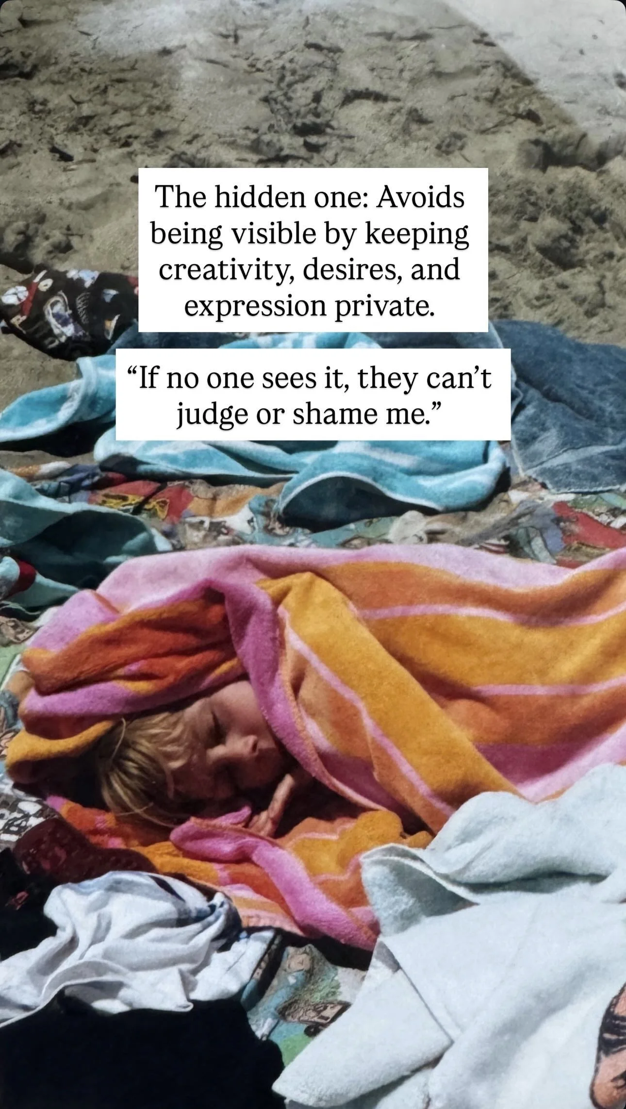 A person sleeping wrapped in an orange, pink, and yellow towel on a blanket, with various towels and clothing items on a sandy surface.